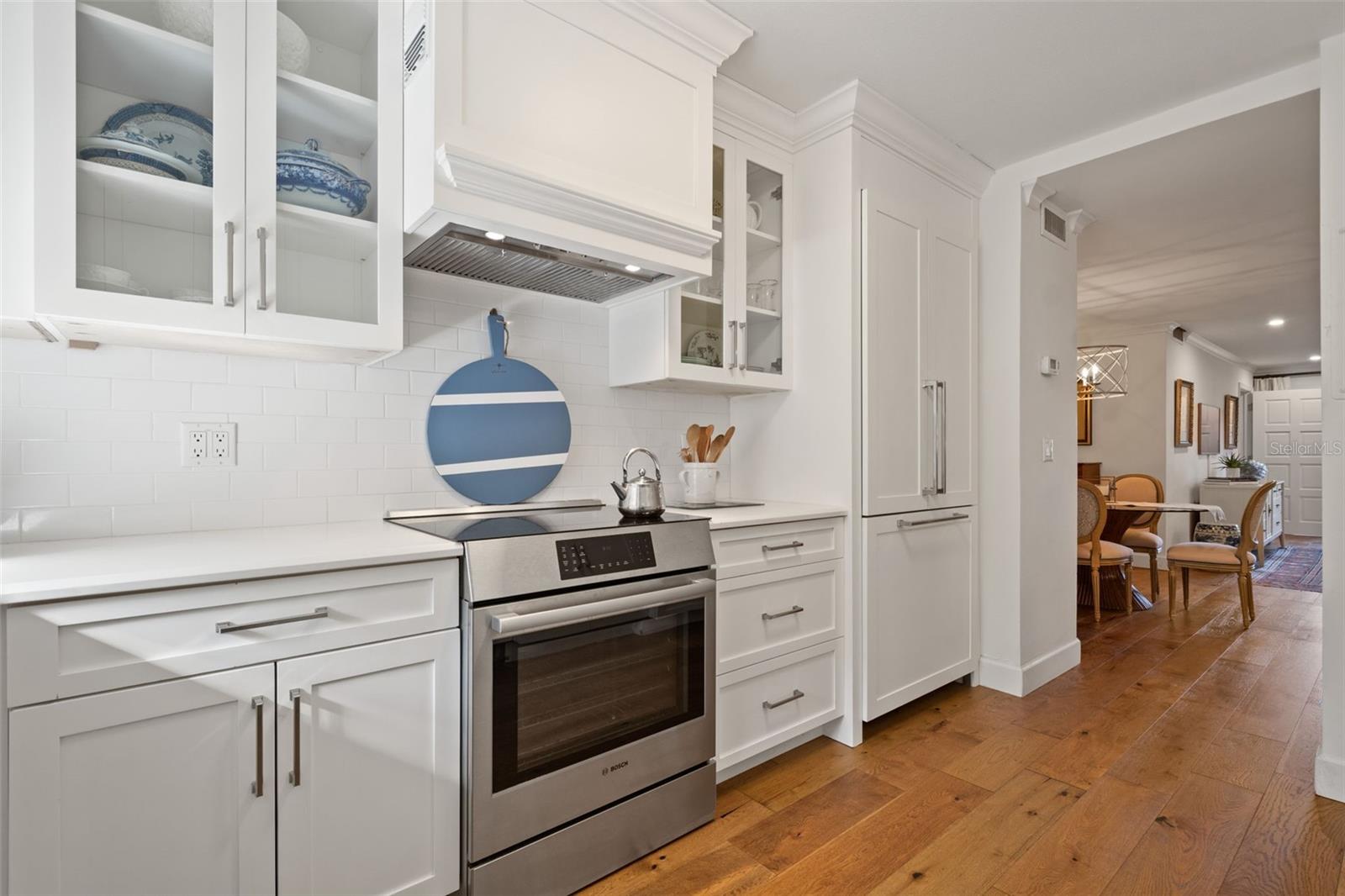 White kitchen with glass-front cabinets, stainless steel range, and a view into the dining area.