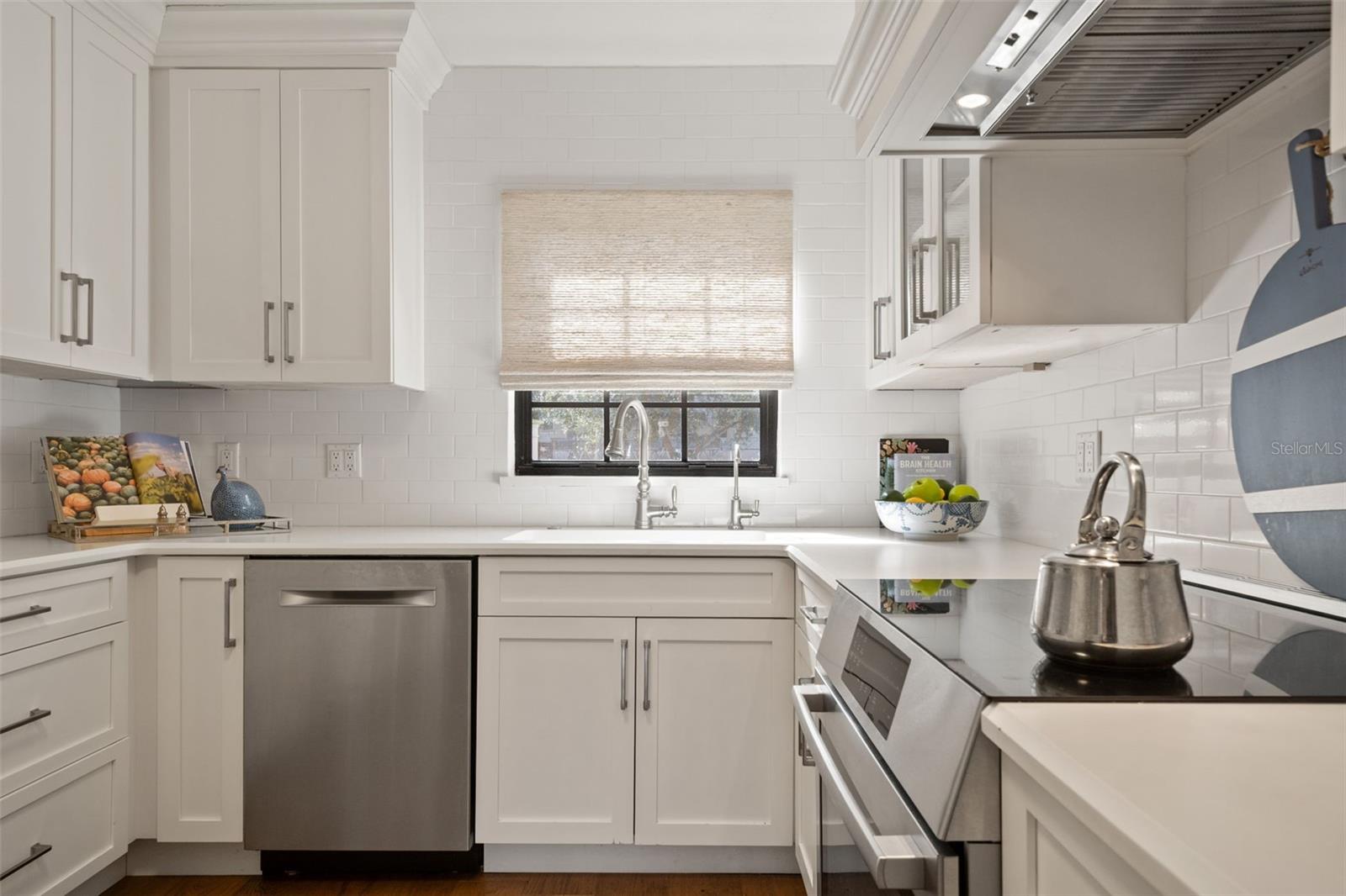Bright white kitchen with shaker cabinets, subway tile, stainless appliances, and a sink beneath a shaded window.