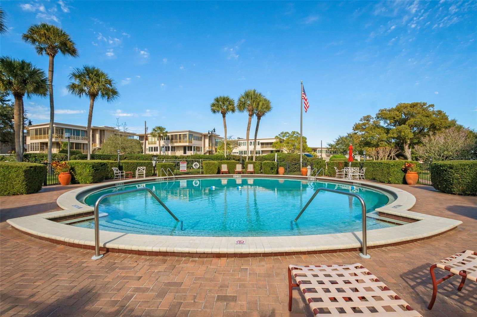 Condominium pool with lounge chairs, palm trees, and residential buildings in the background.