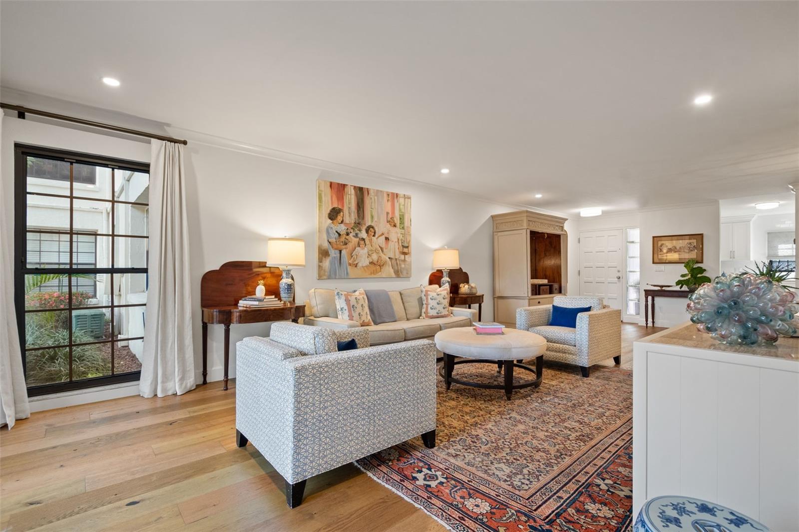 Furnished living room with pale sofas, a patterned rug, and a large black-framed window.