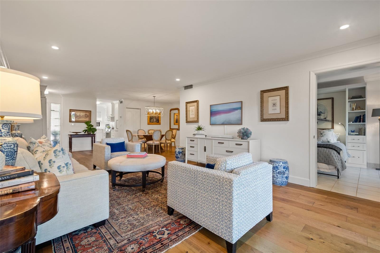 Living room with patterned rugs and pale seating, opening to a dining area and bedroom.
