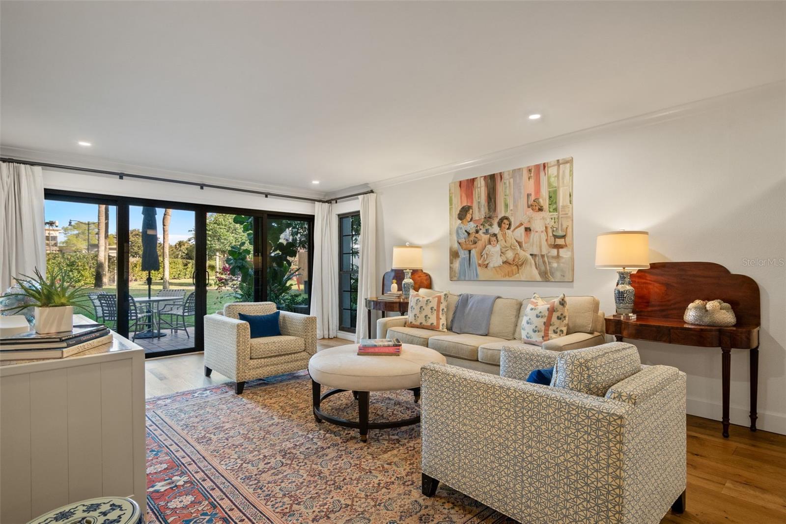 Living room with patterned armchairs, a colorful rug, and sliding doors opening to a garden.