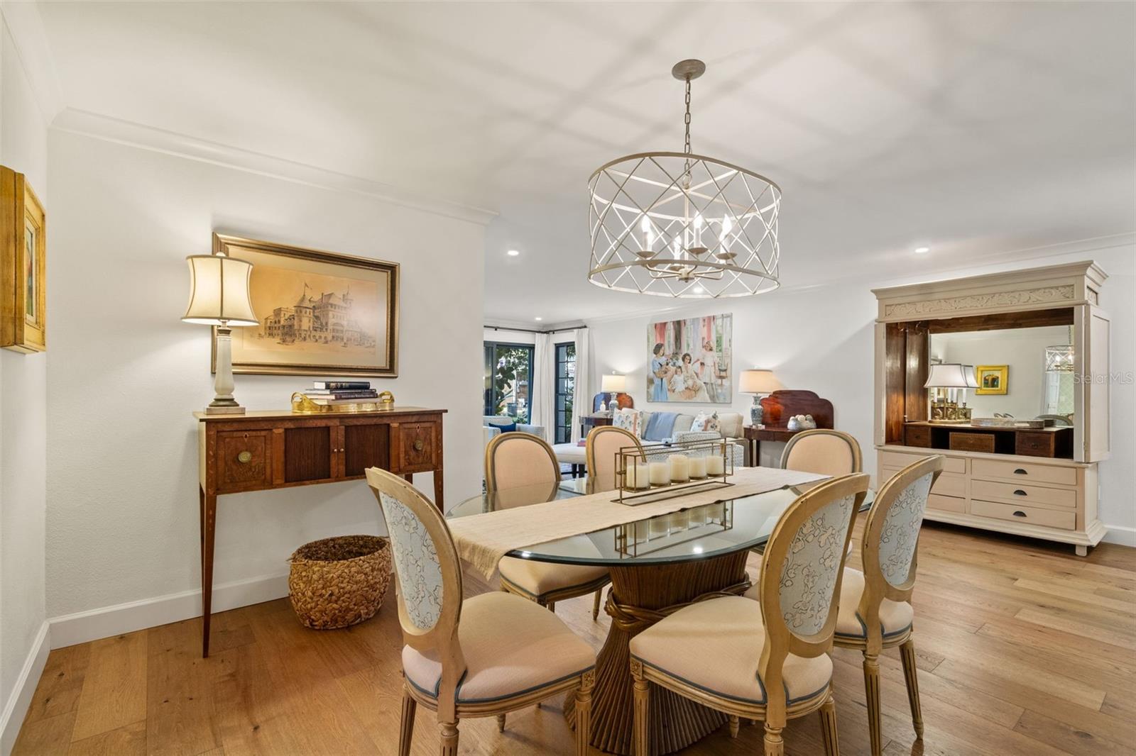 Dining room with a glass-top table, upholstered chairs, geometric chandelier, and view into the living area.