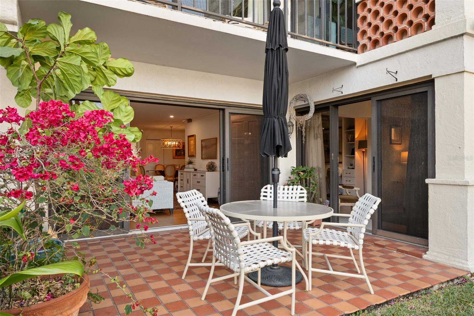 Tiled patio furnished with white chairs and a round table, framed by flowering bougainvillea.