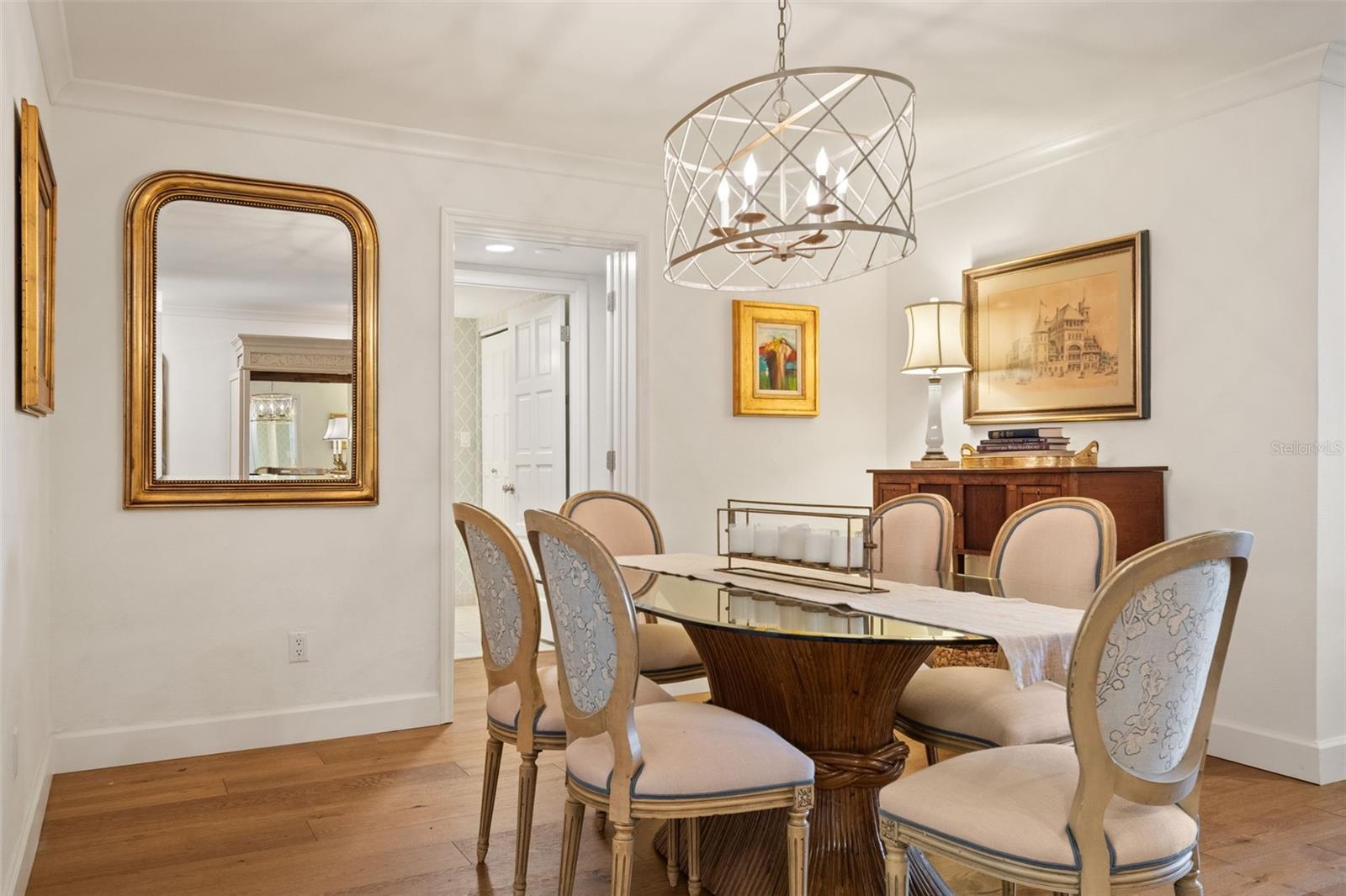 Dining room with an oval glass-top table, upholstered chairs, chandelier, and hardwood floors.