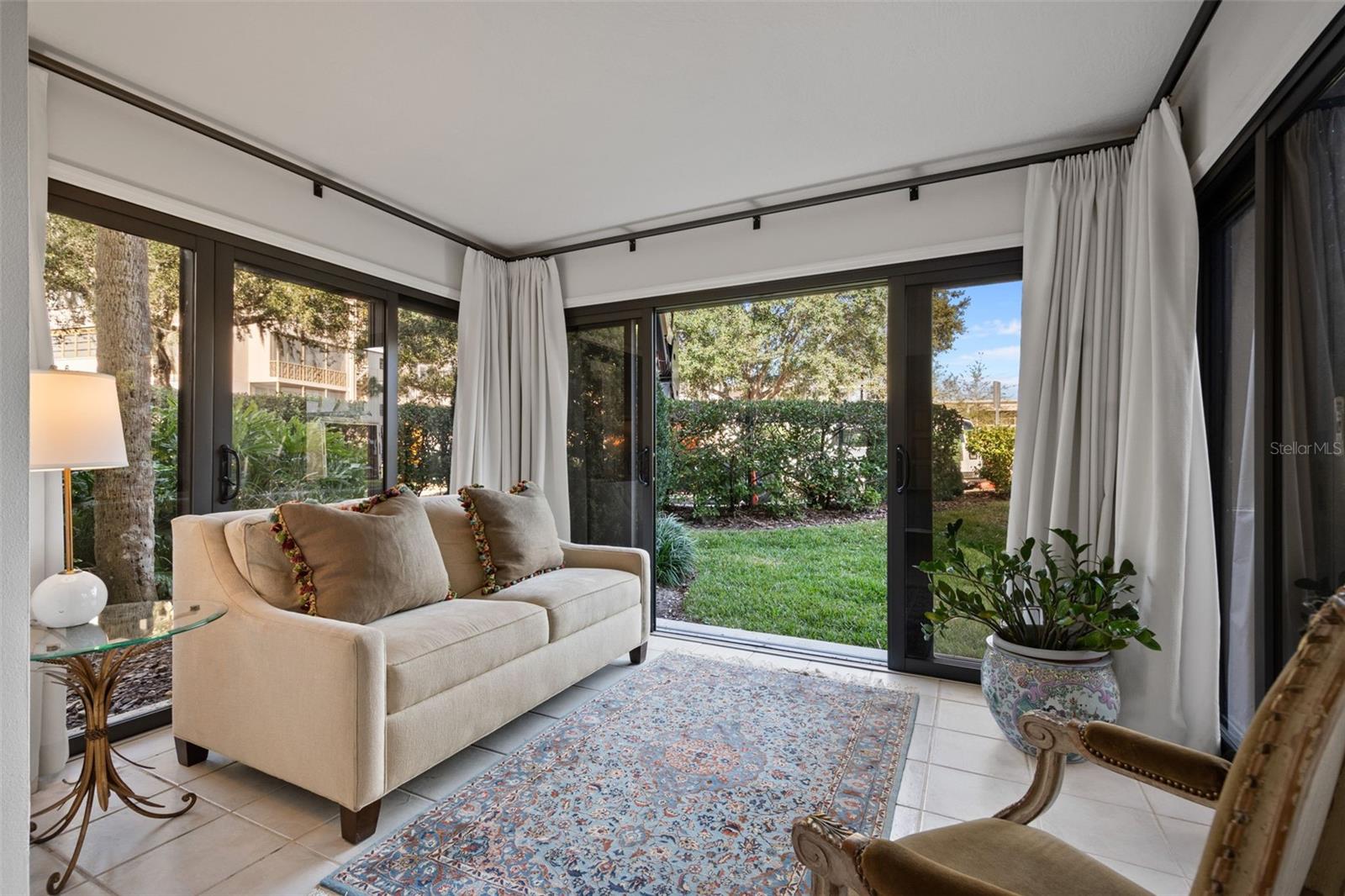 Sunroom with a cream sofa, patterned rug, and glass doors opening onto a garden.