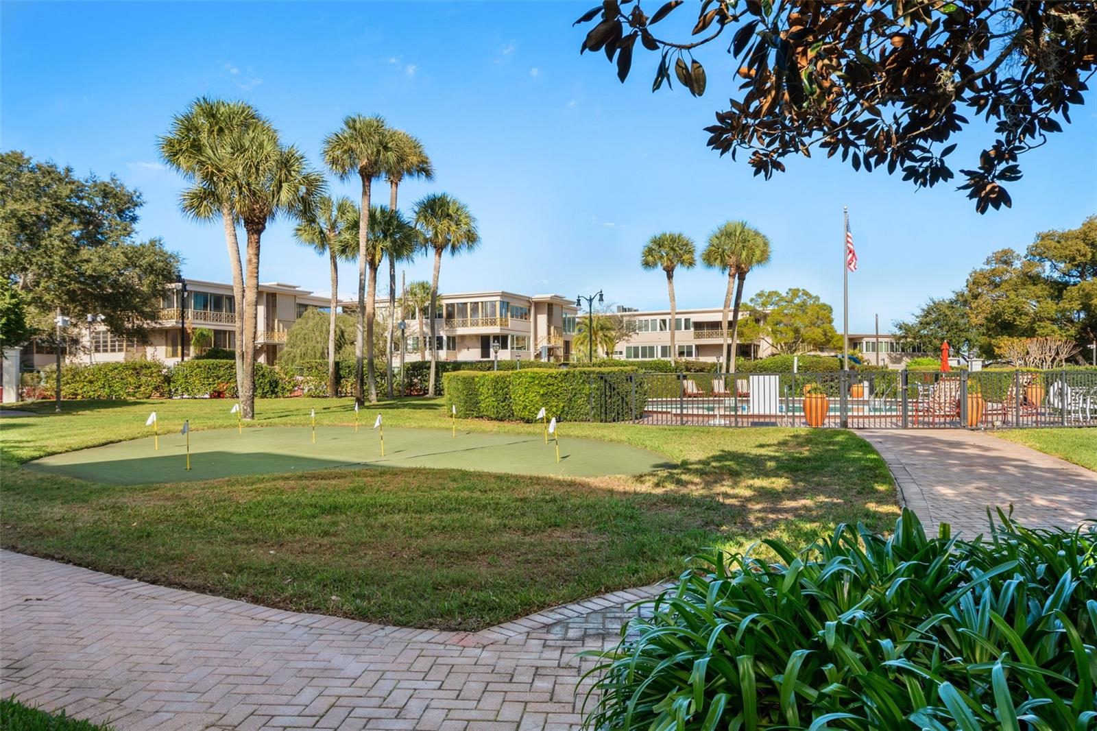 Condominium grounds with a fenced pool, palm trees, and a small putting green.