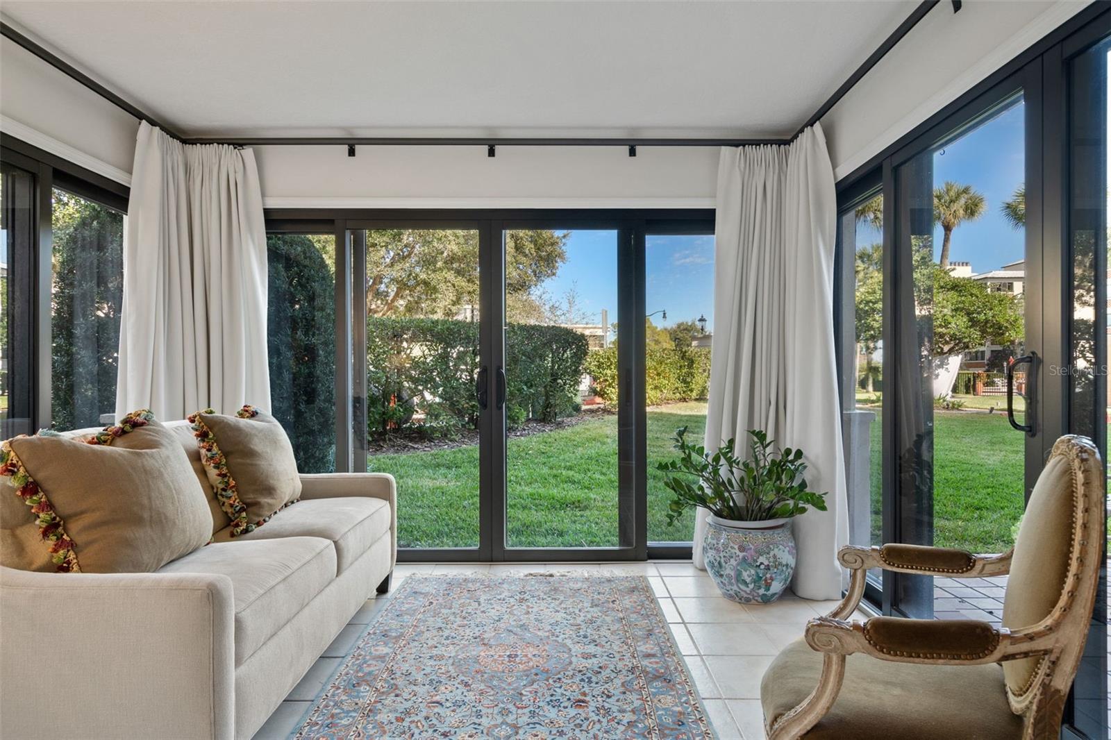 Sunroom with a cream sofa, patterned rug, and broad glass doors overlooking a grassy garden.