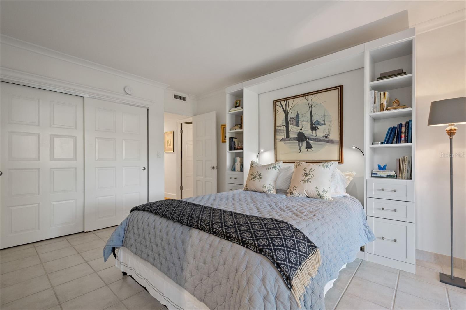 Bedroom with pale blue bedding, built-in bookshelves, and sliding closet doors.