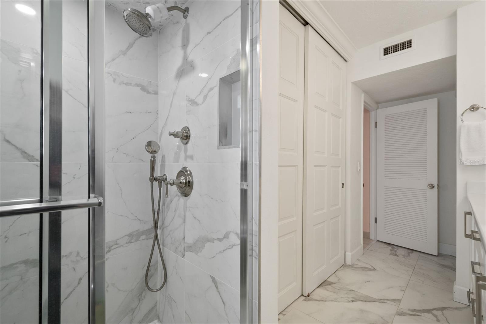 Bathroom with a glass-enclosed marble-look tile shower and chrome fixtures.