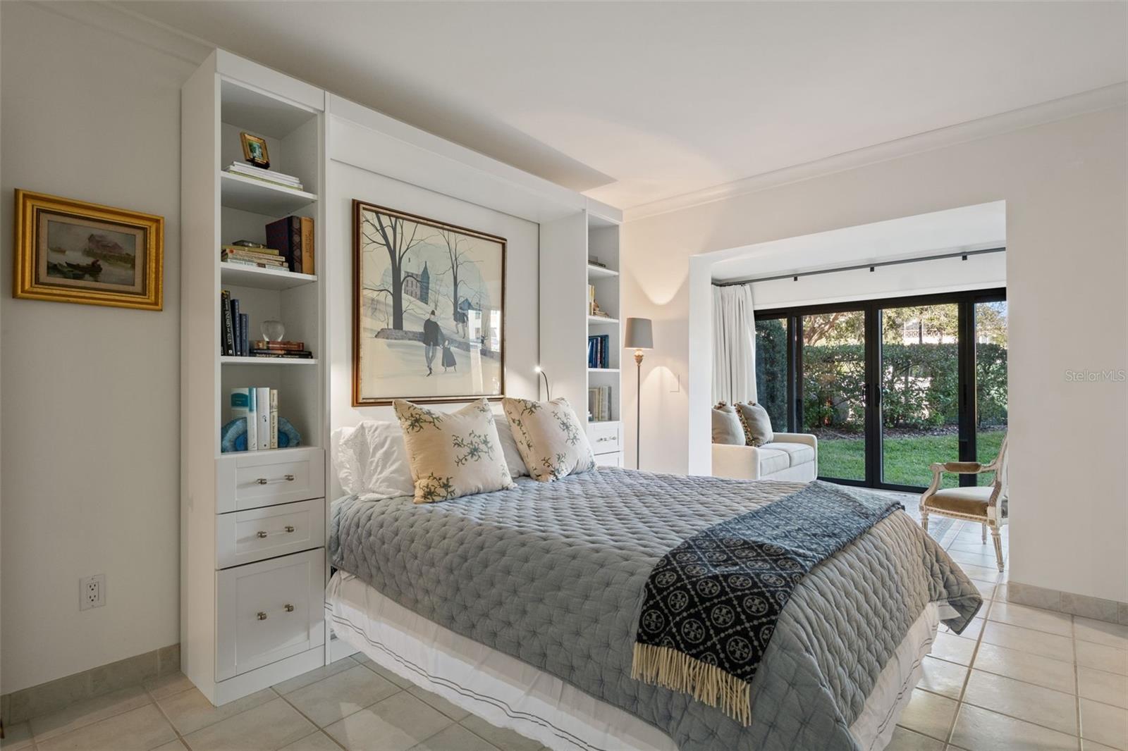 Bedroom with built-in bookshelves and glass doors opening to a garden.