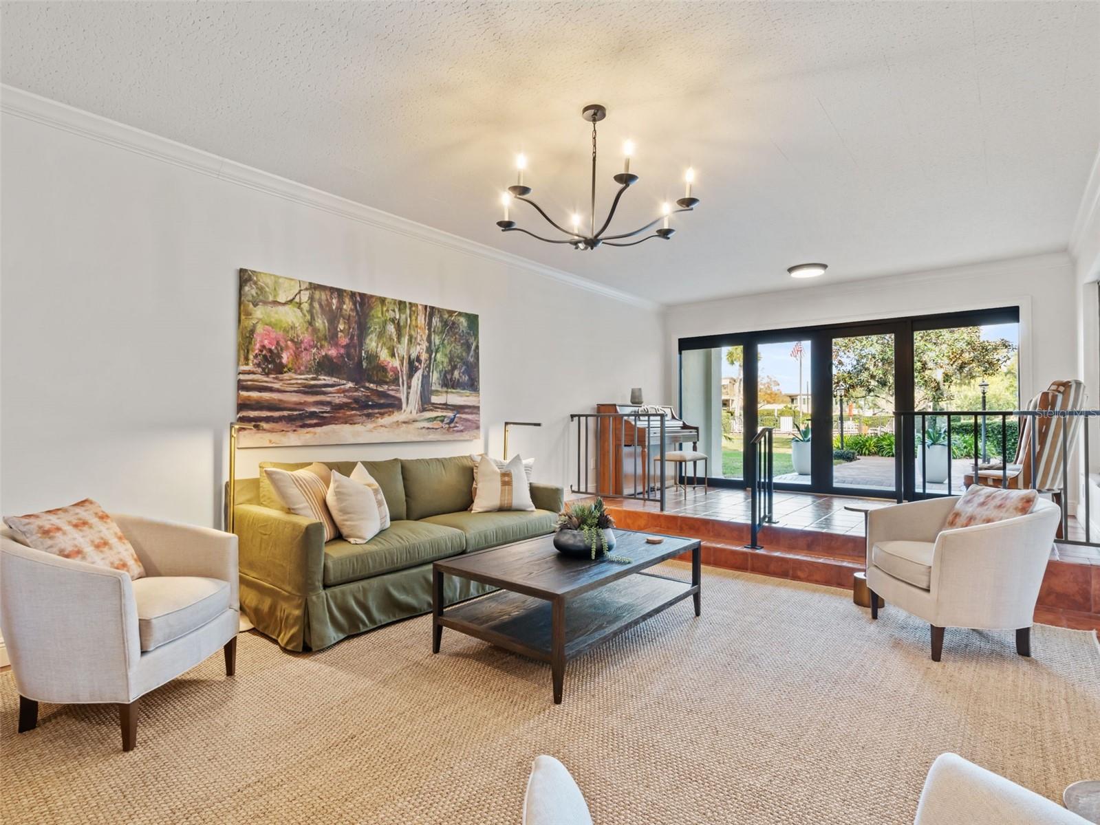Staged living room with a green sofa and black-framed glass doors opening to a patio.