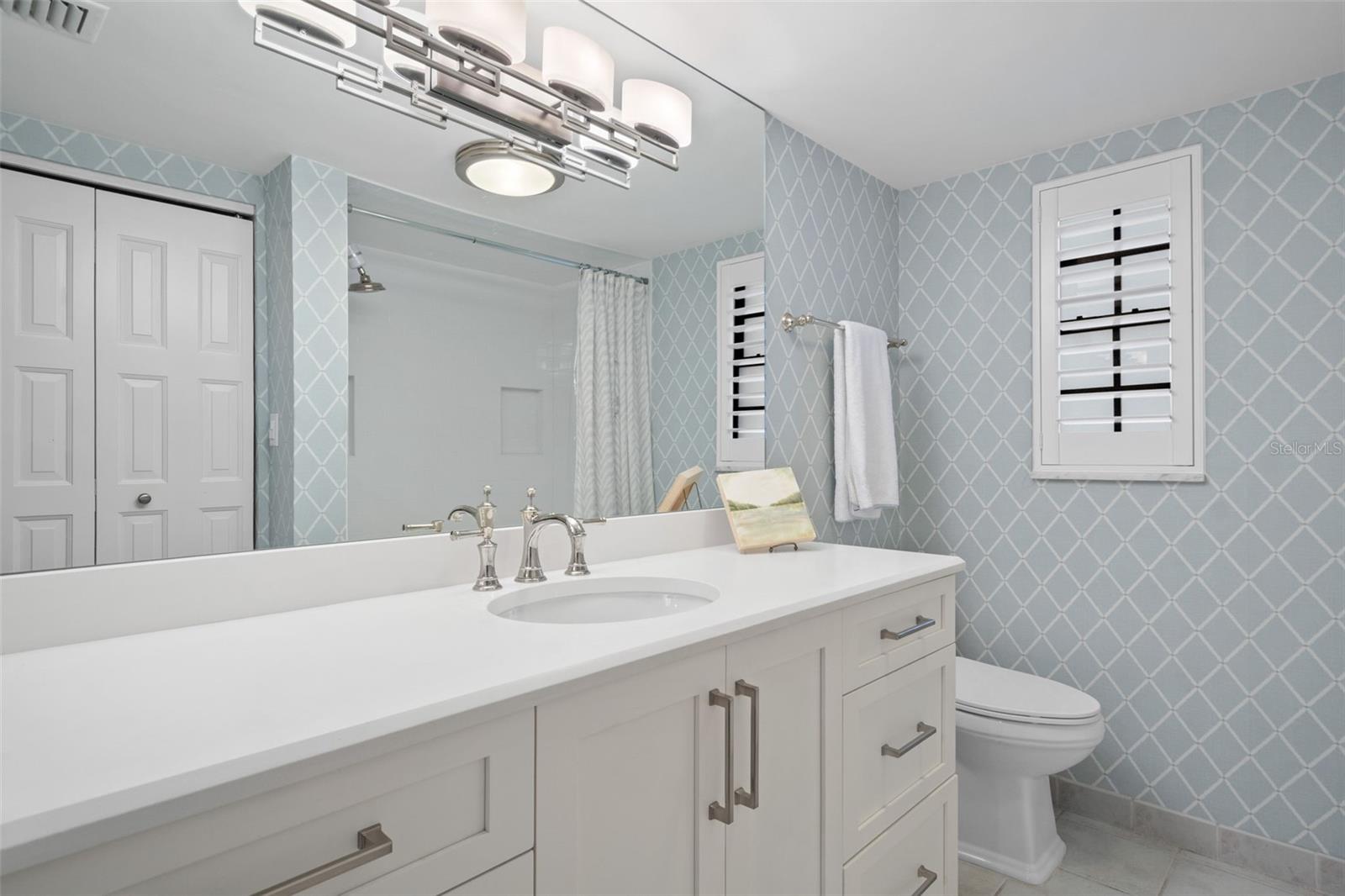 Bathroom with a white vanity and sink, blue geometric-patterned walls, and plantation shutters.