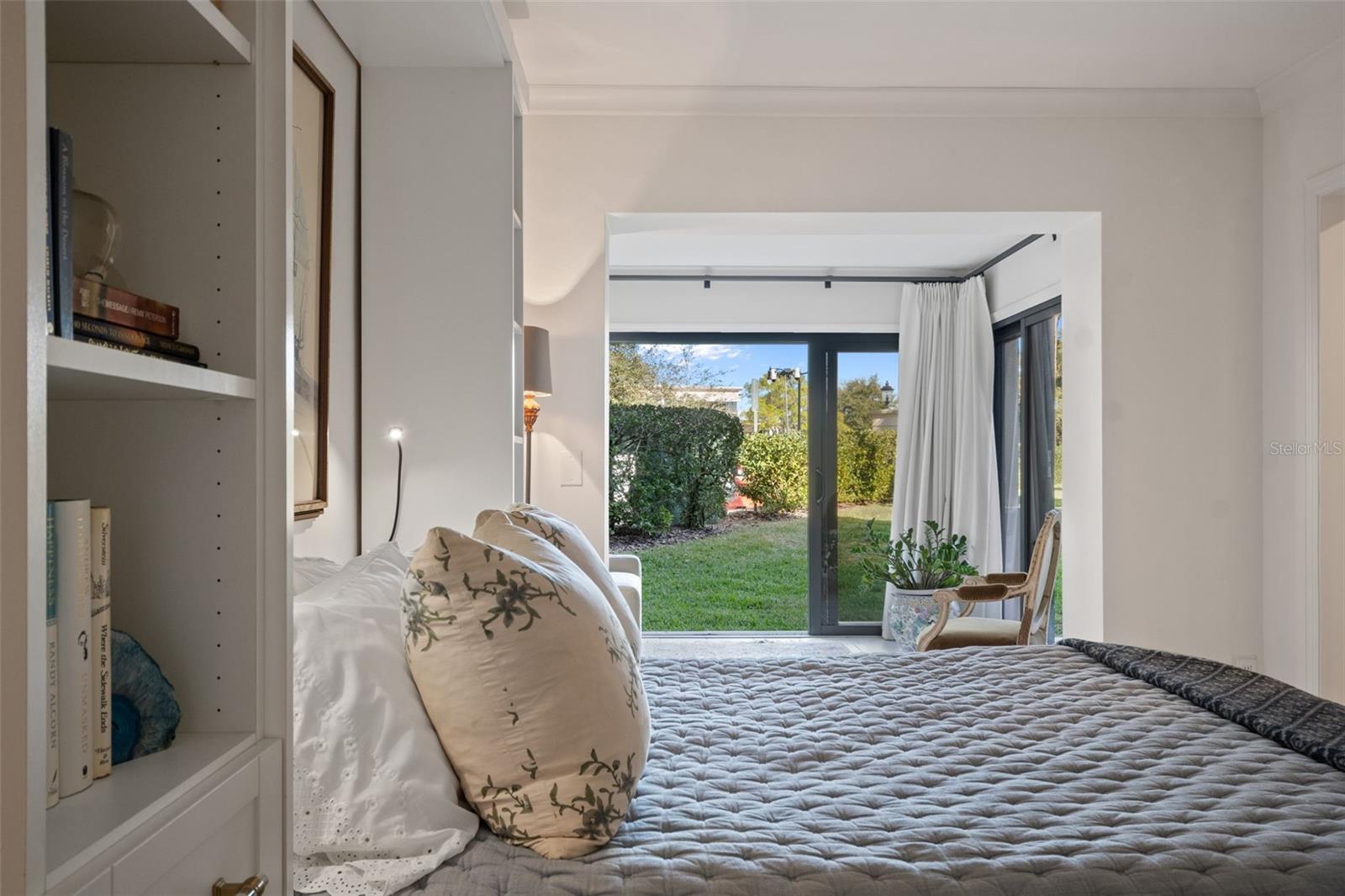 Bedroom with built-in shelving and sliding glass doors opening onto a grassy garden.