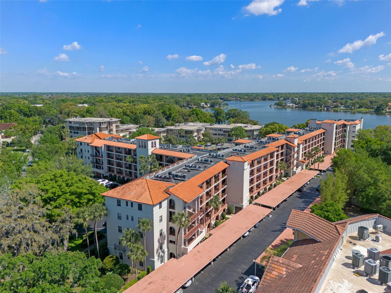 Aerial view of condominium buildings with red tile roofs beside a lake.