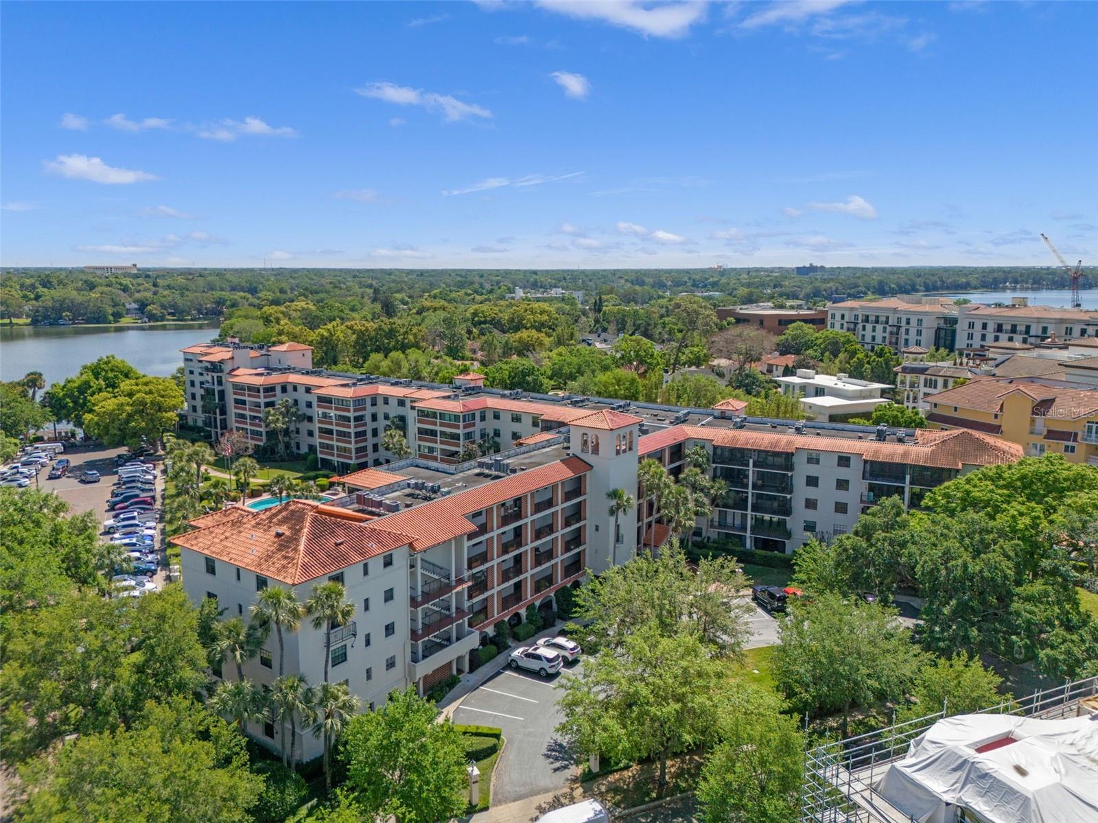Aerial view of terracotta-roofed condominiums among trees, with a lake in the distance.