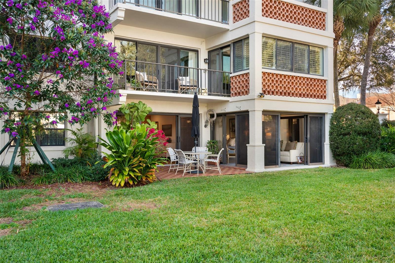 Residence exterior with a brick patio, upper balconies, terracotta screens, and tropical landscaping.