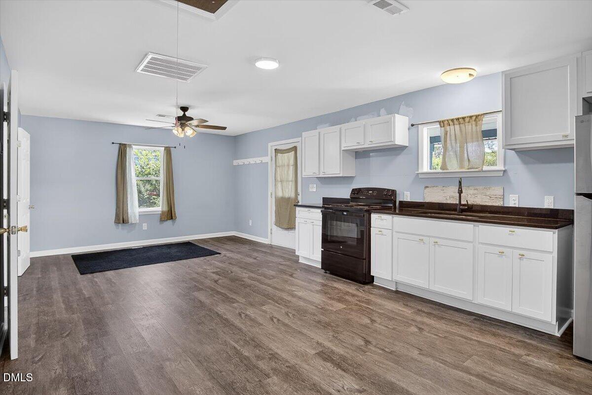 Kitchen with white cabinets, dark countertops, black range, and wood-look flooring.