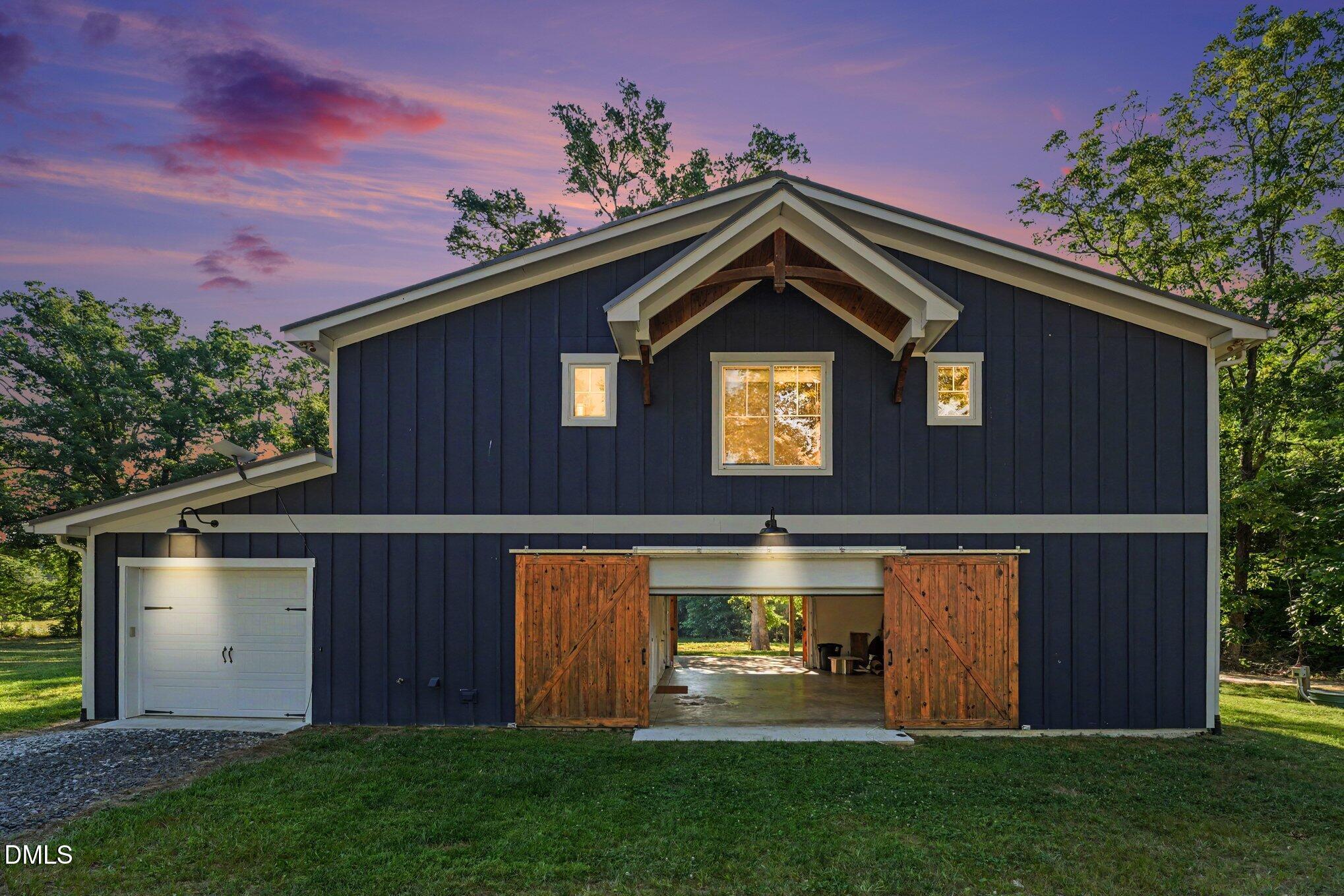 Navy barn-style garage with open wooden sliding doors beneath a pink dusk sky.