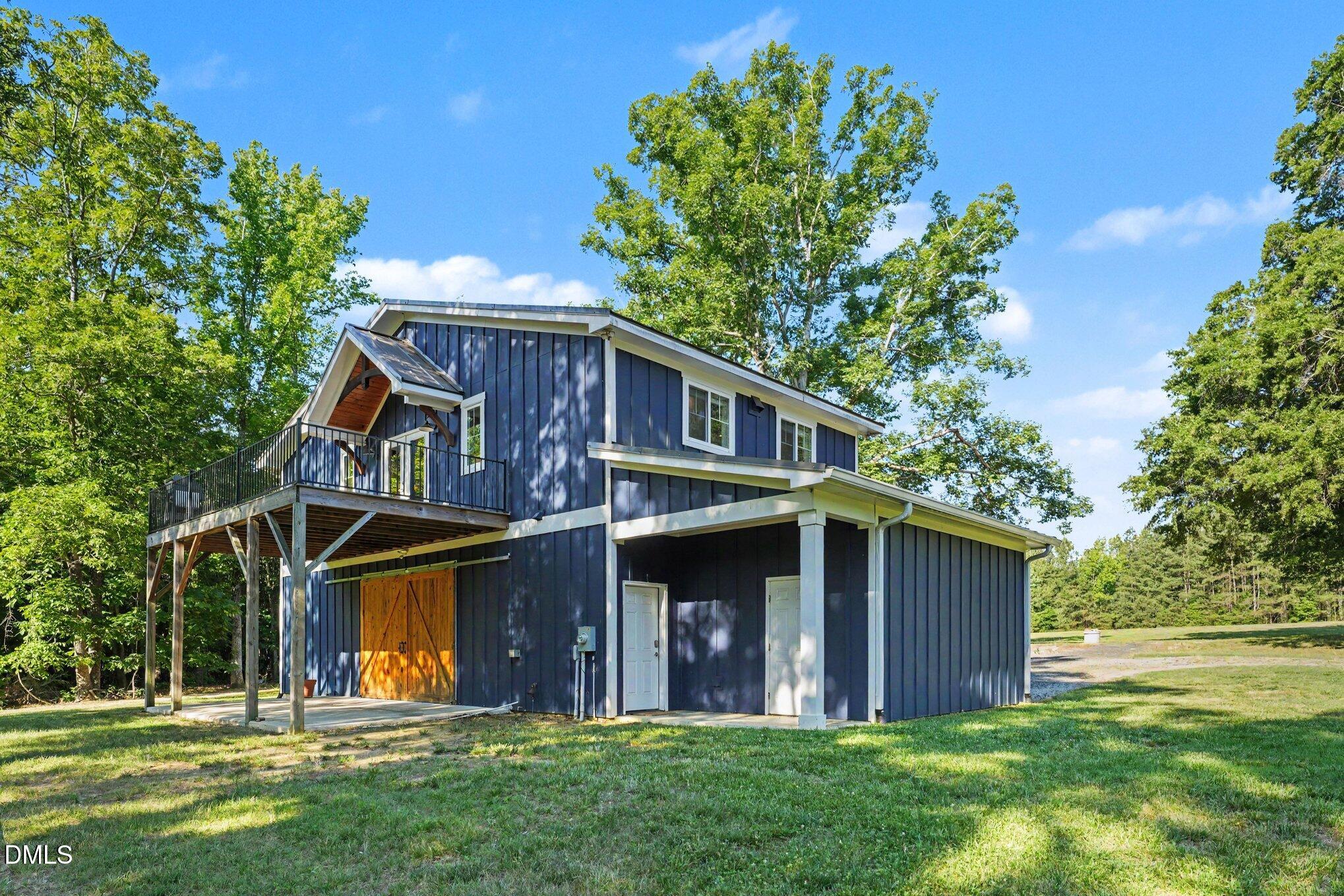 Blue barn-style home with a raised deck, timber supports, and large wooden double doors.