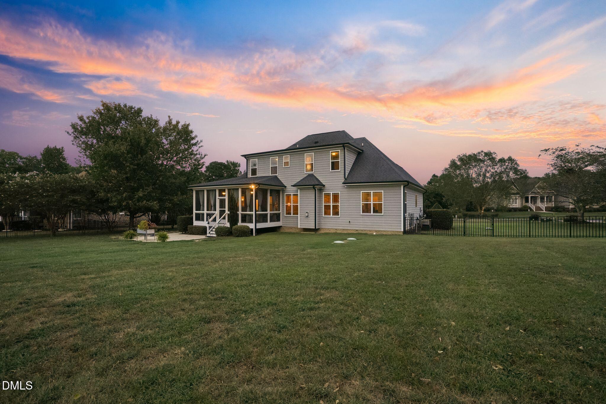 Two-story gray house with a screened porch and broad lawn beneath a pink sunset sky.