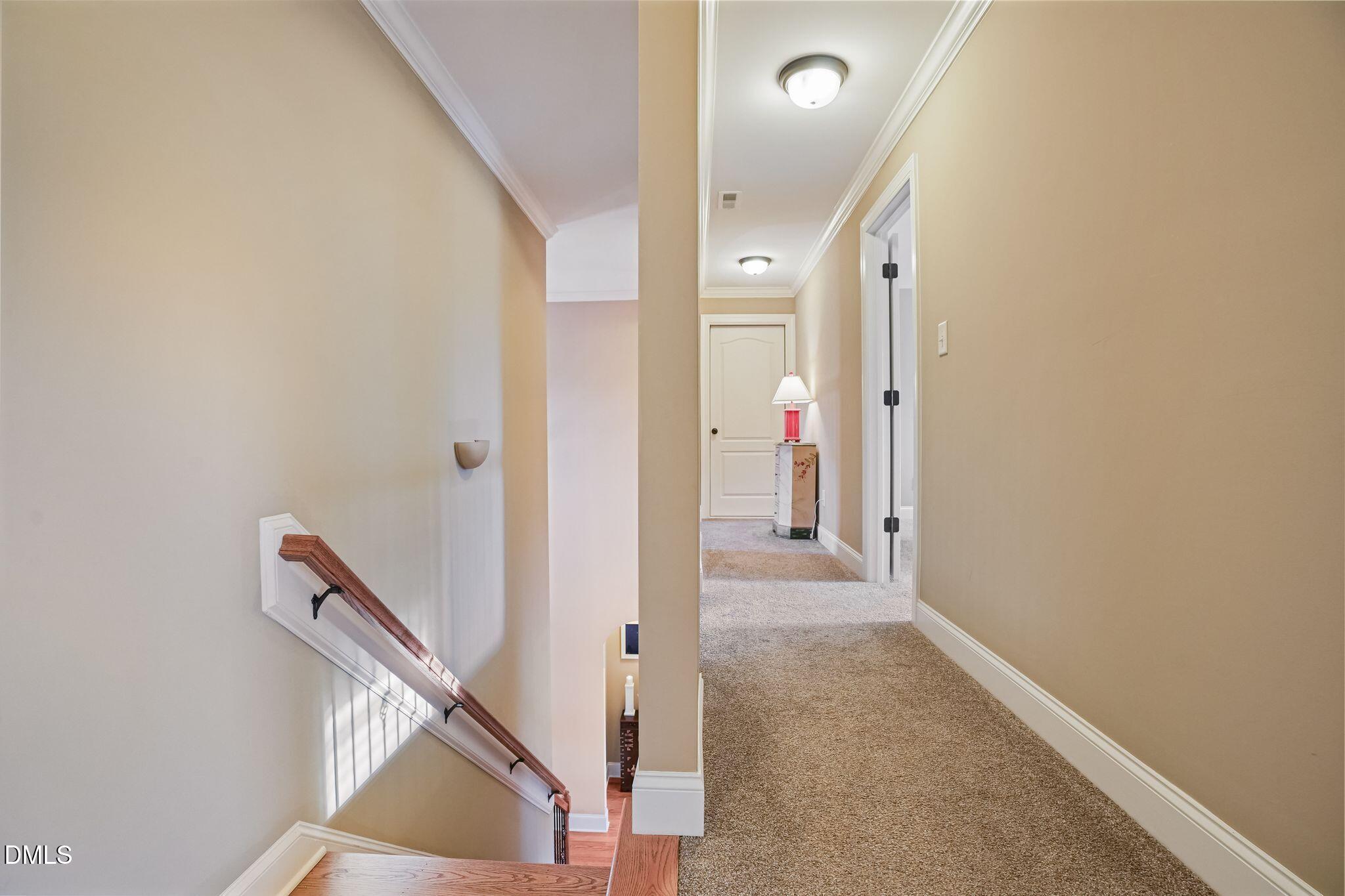 Upstairs hallway with carpet, a red lamp on a console table, and an adjacent stairwell.