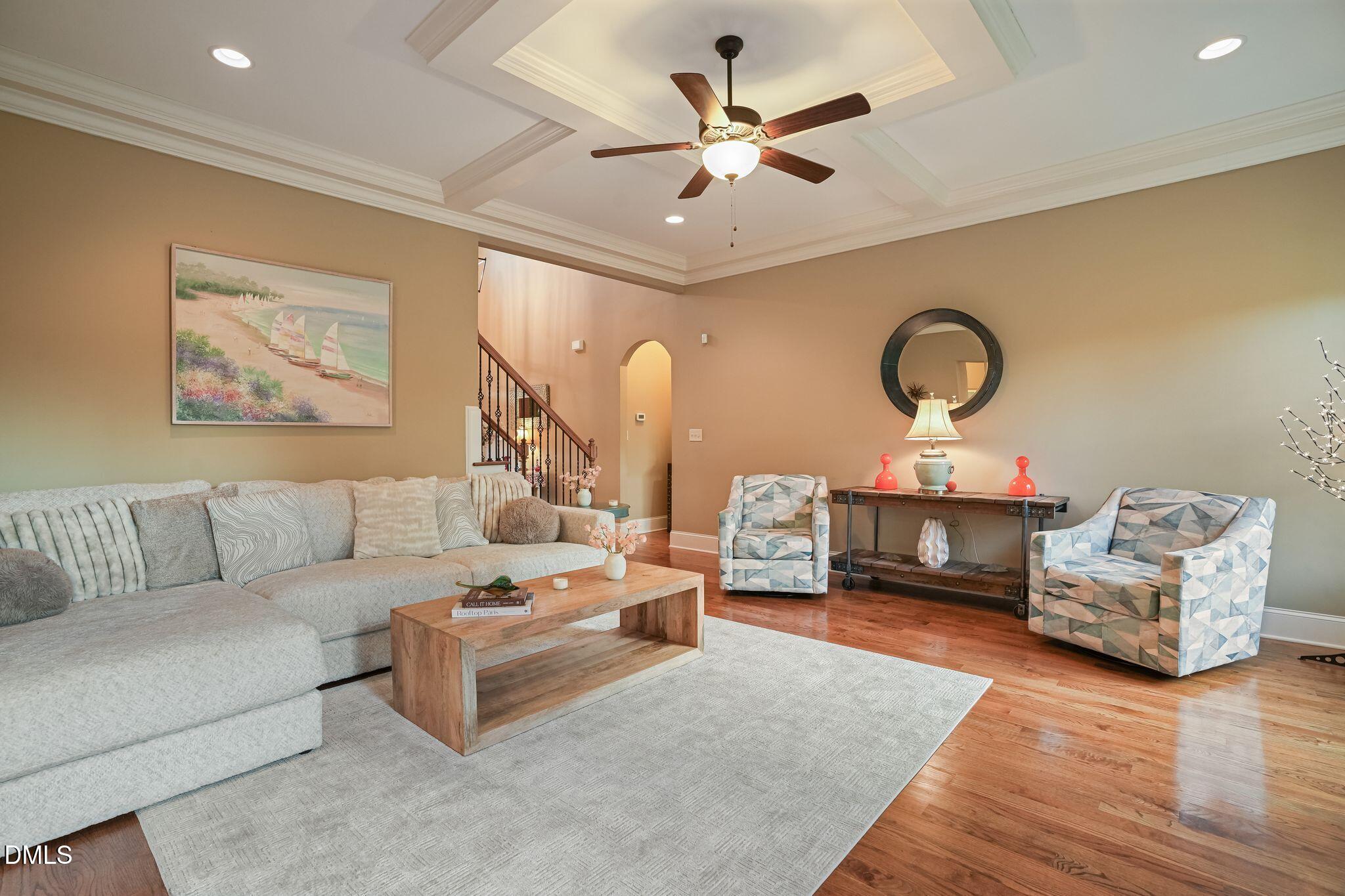 Living room with a large gray sectional, patterned armchairs, hardwood floors, and a tray ceiling with a fan.