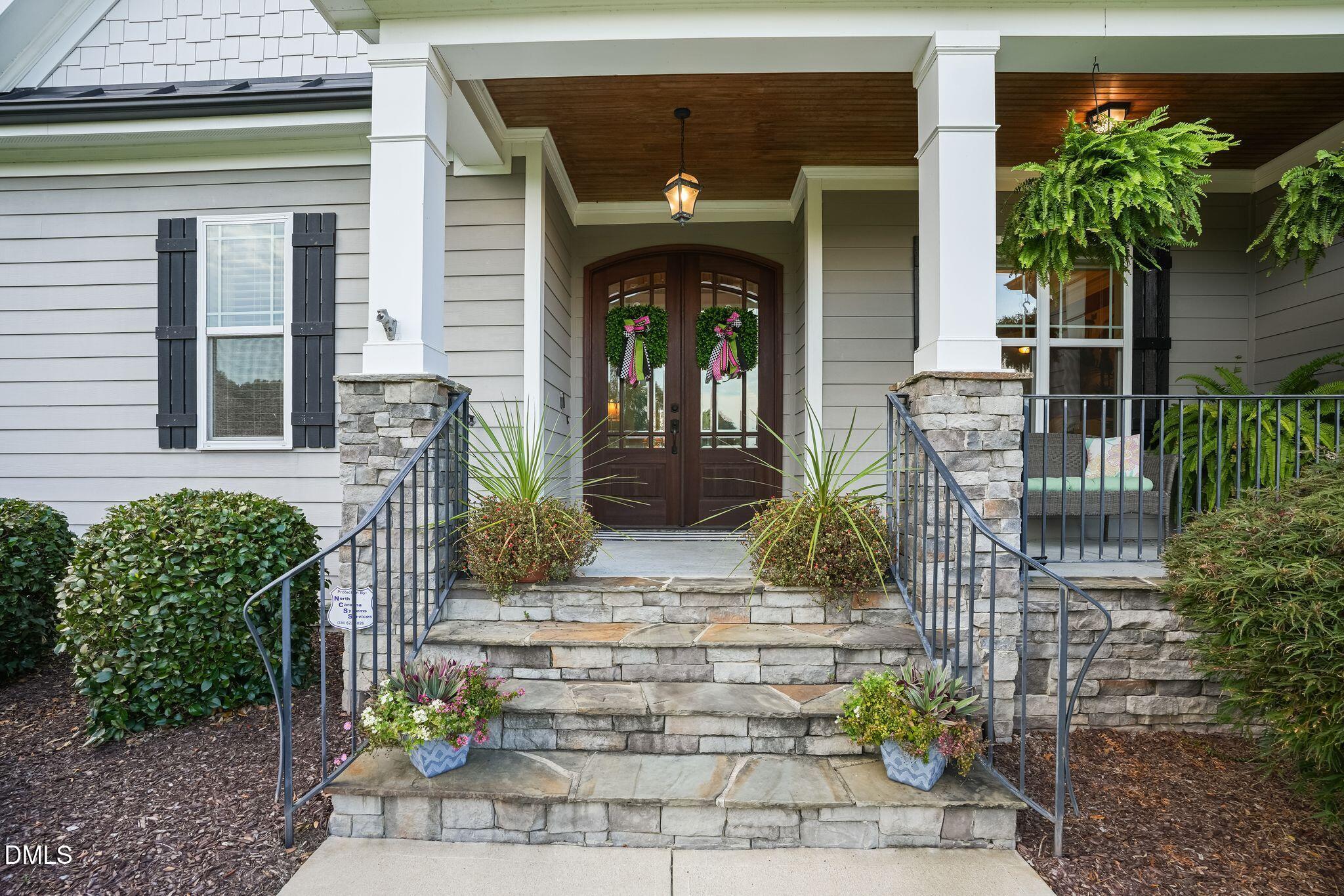 Home entrance with stone steps, covered porch, dark wood double doors, and potted flowers.