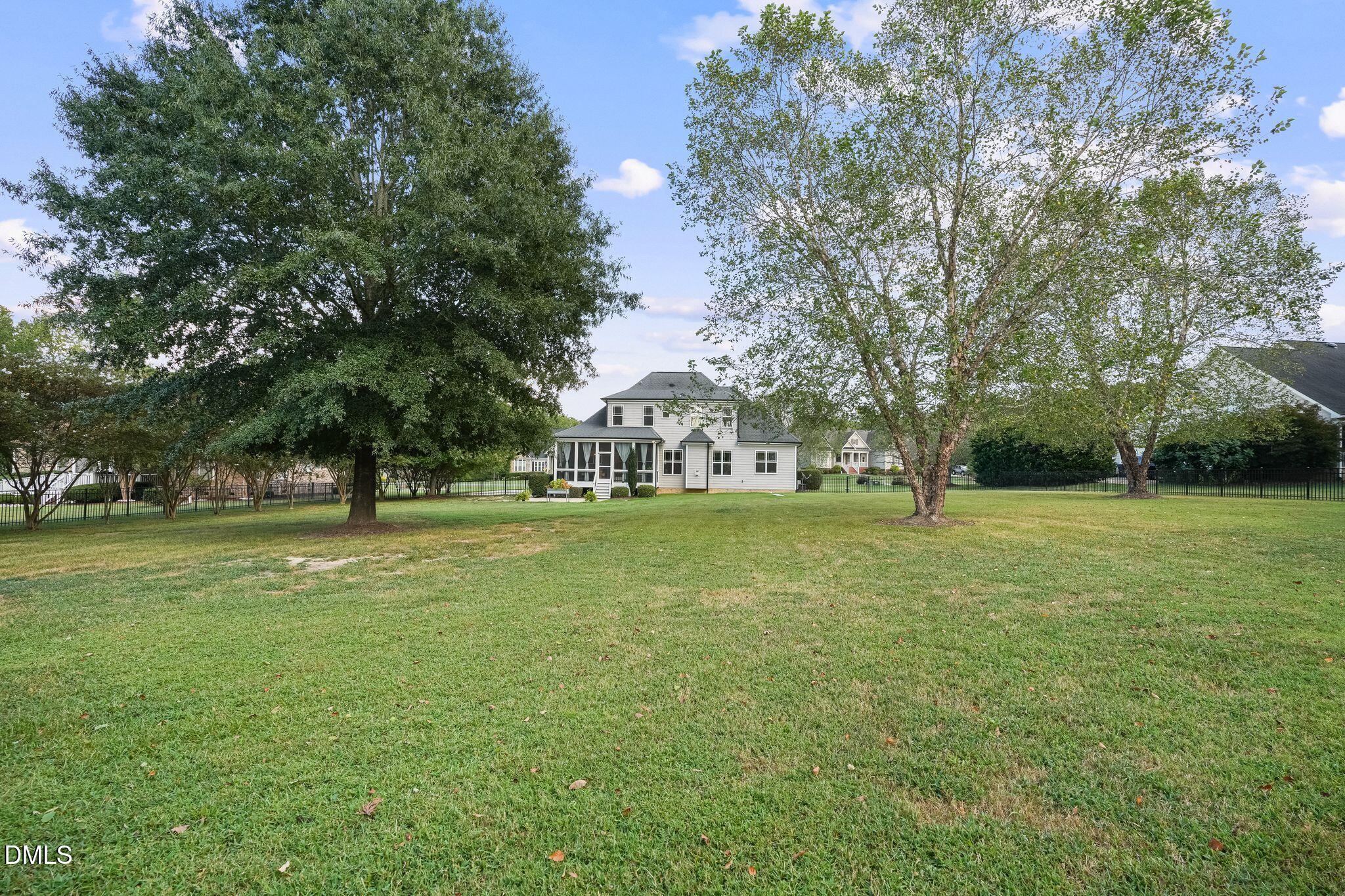 Rear of a two-story house beyond a broad lawn, framed by mature trees and a screened porch.