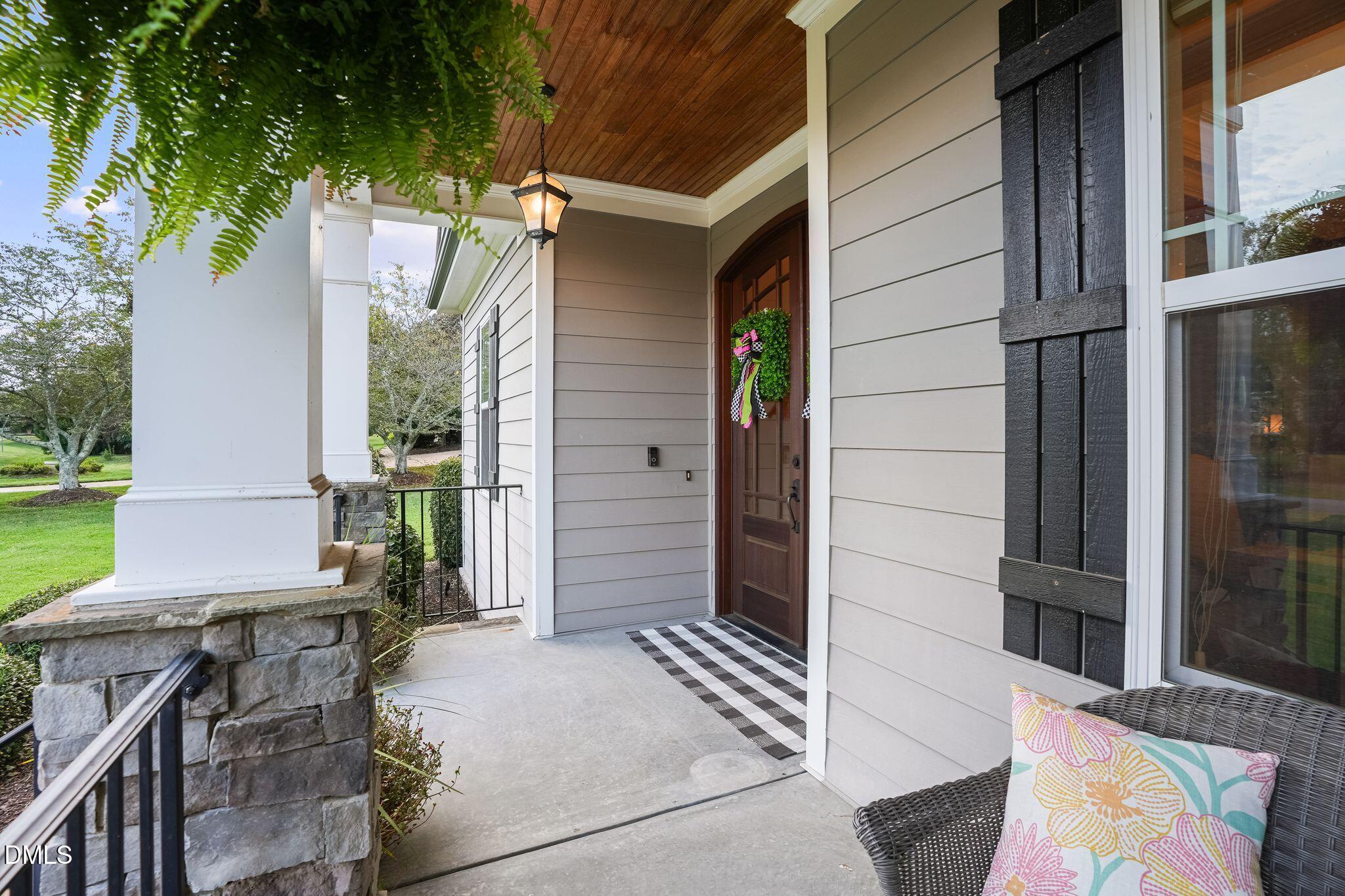 Covered front porch with a wood-plank ceiling, stone columns, and a wreath on the entry door.