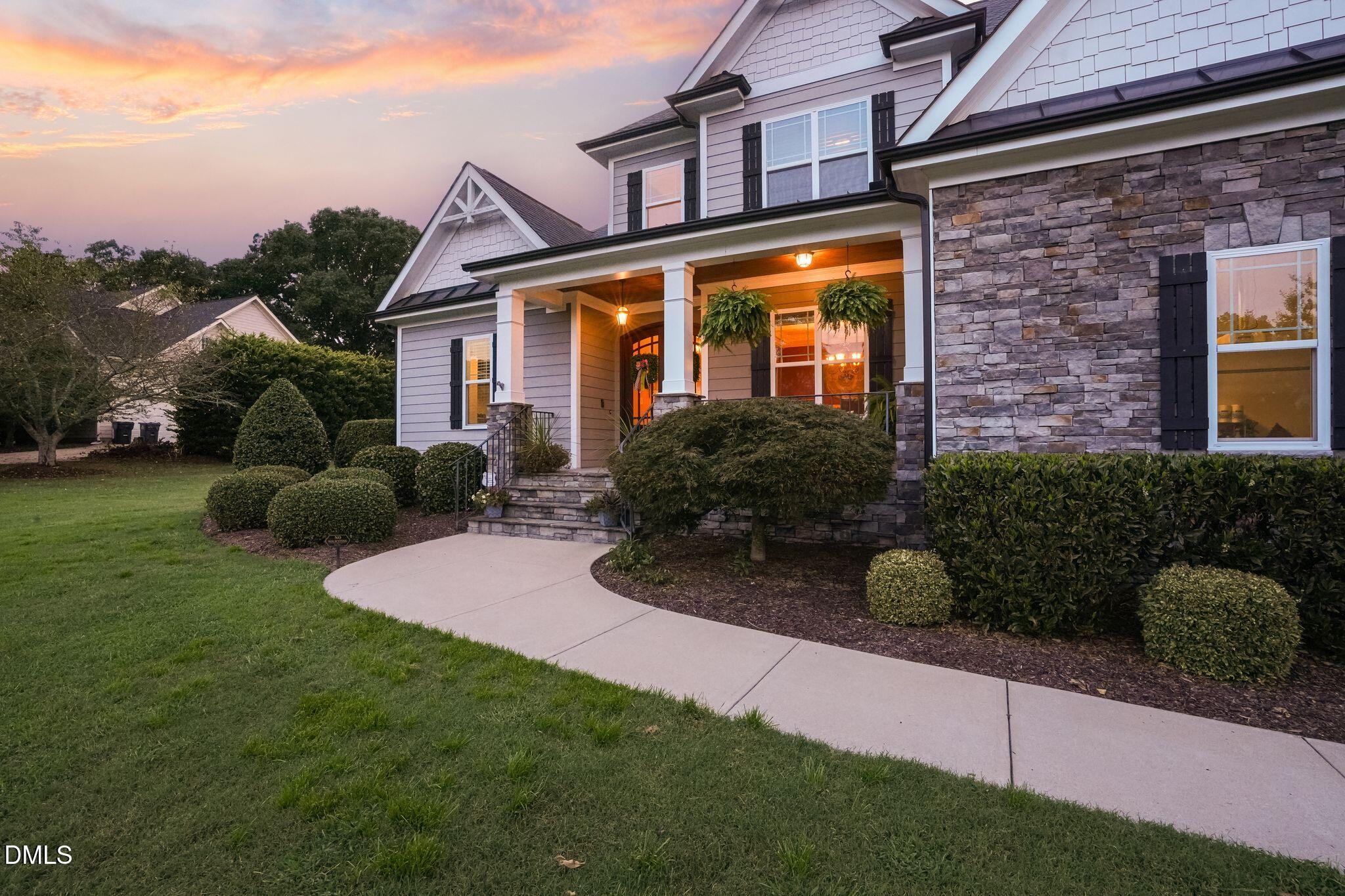 Two-story gray home with stone facade, covered porch, and landscaped front yard at dusk.