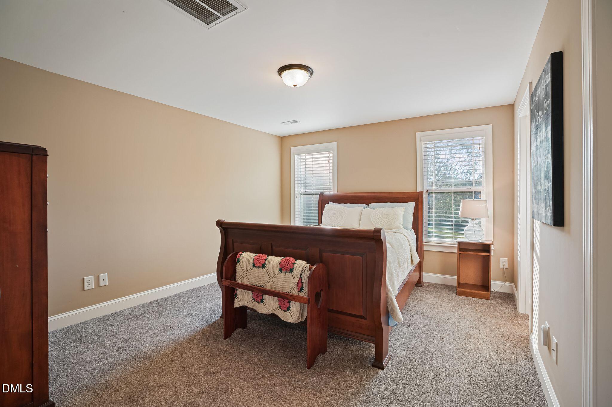 Furnished bedroom with a dark wood bed, white bedding, gray carpet, and two windows with blinds.
