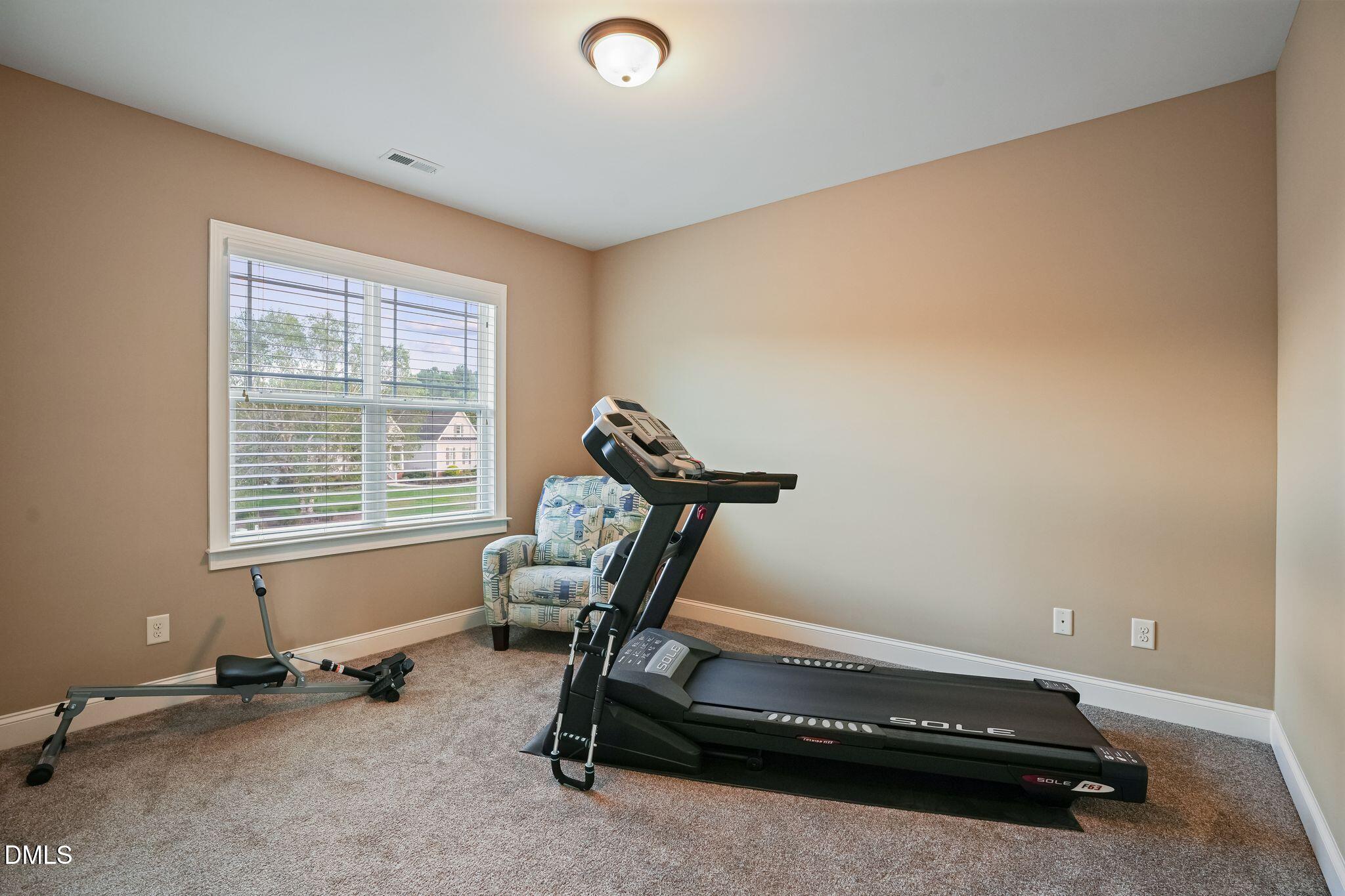 Home exercise room with a treadmill and rowing machine beside a large window.