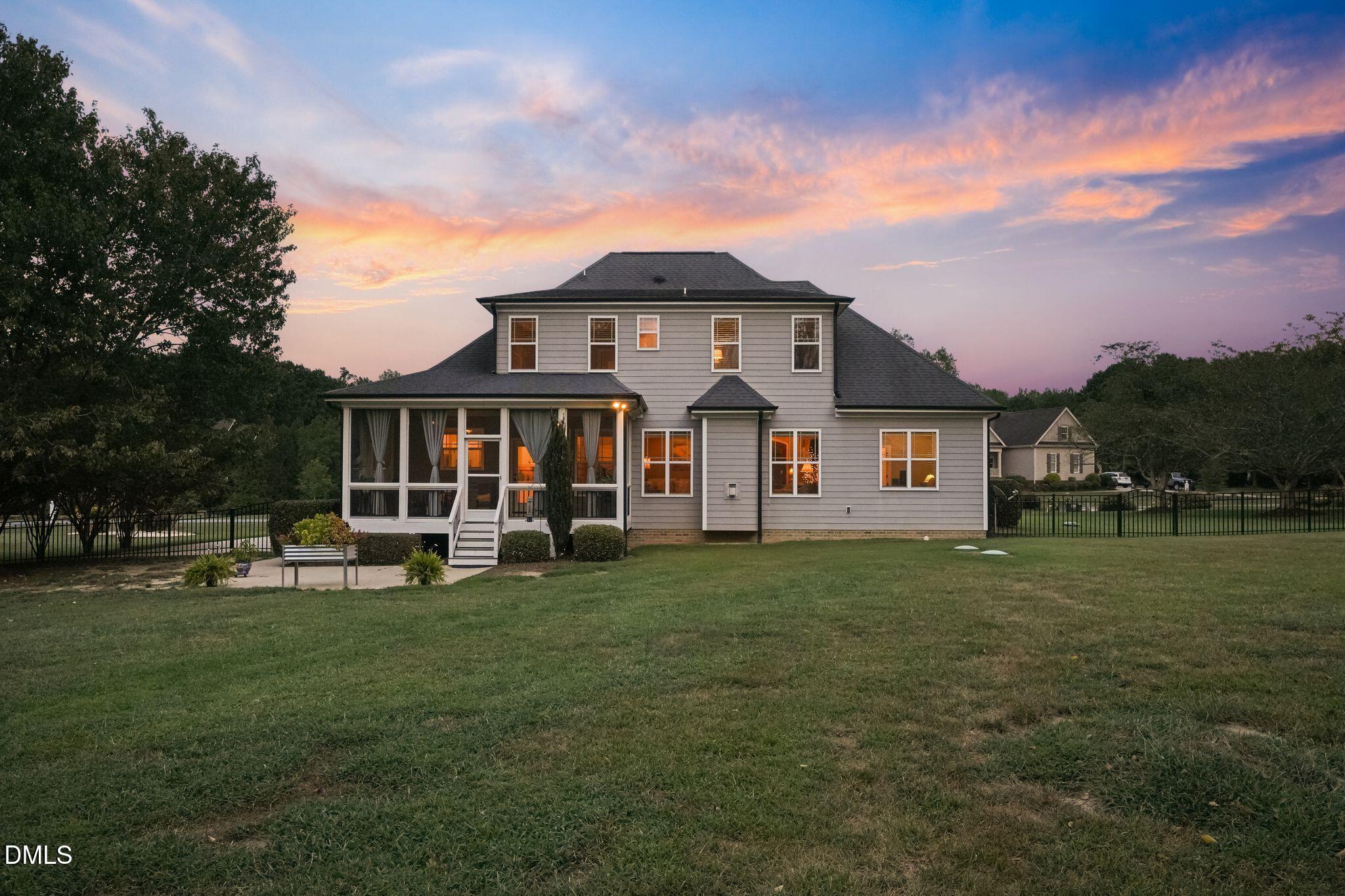Two-story gray house with a screened porch and fenced lawn at dusk.