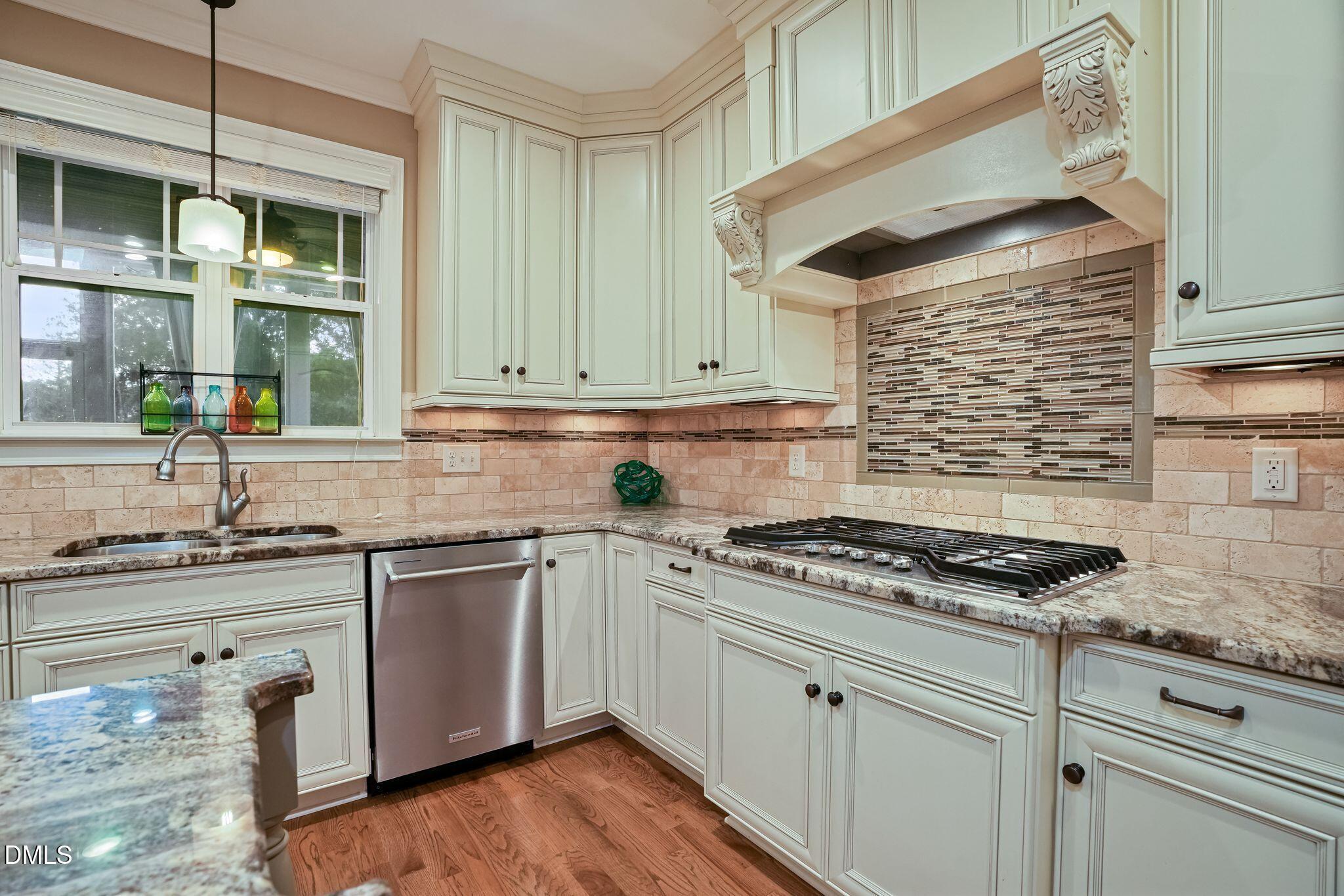 Kitchen with white paneled cabinets, granite counters, and a gas cooktop beneath a decorative range hood.