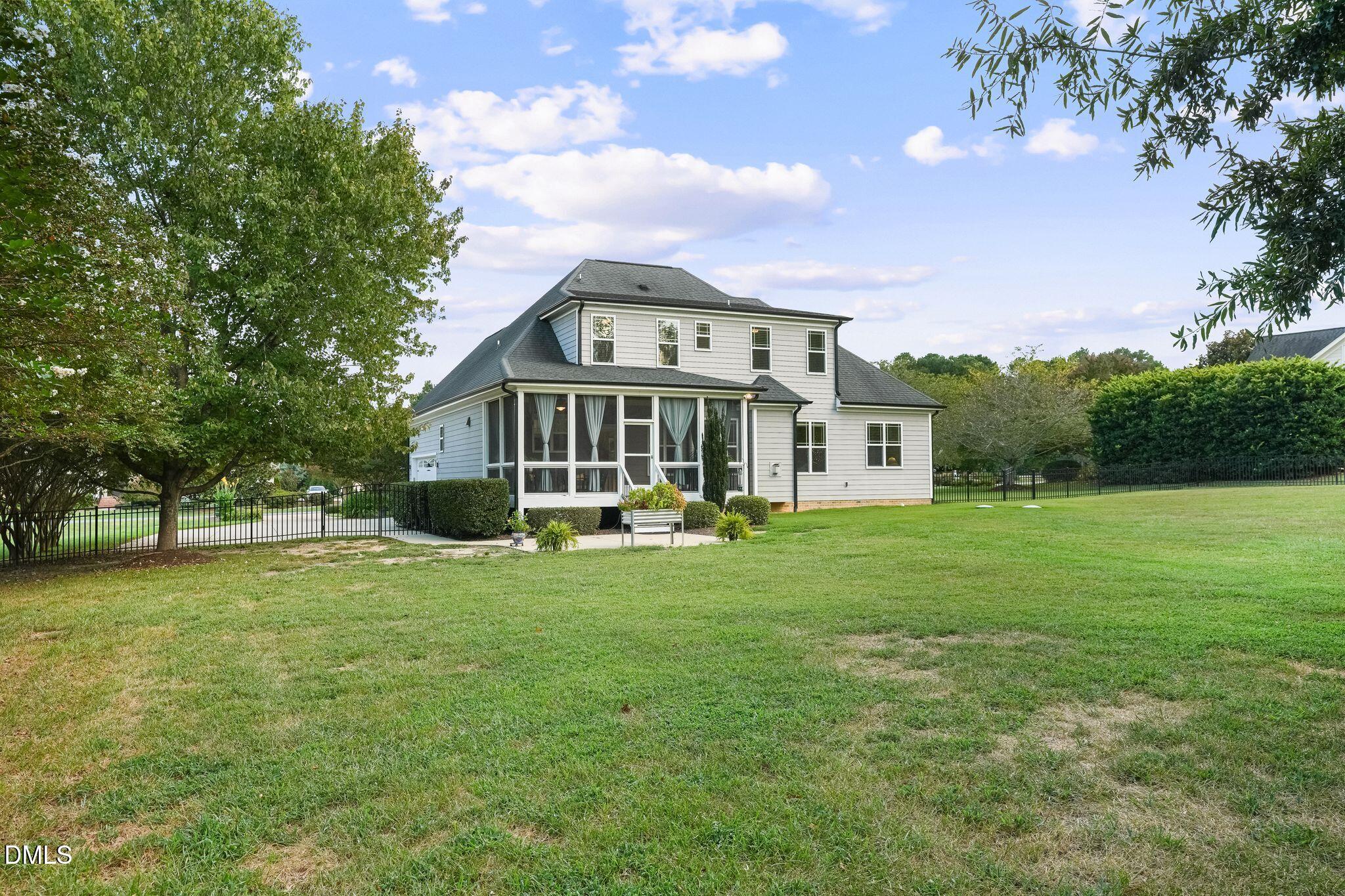 Two-story gray house with a screened porch, black metal fence, and broad grassy lawn.