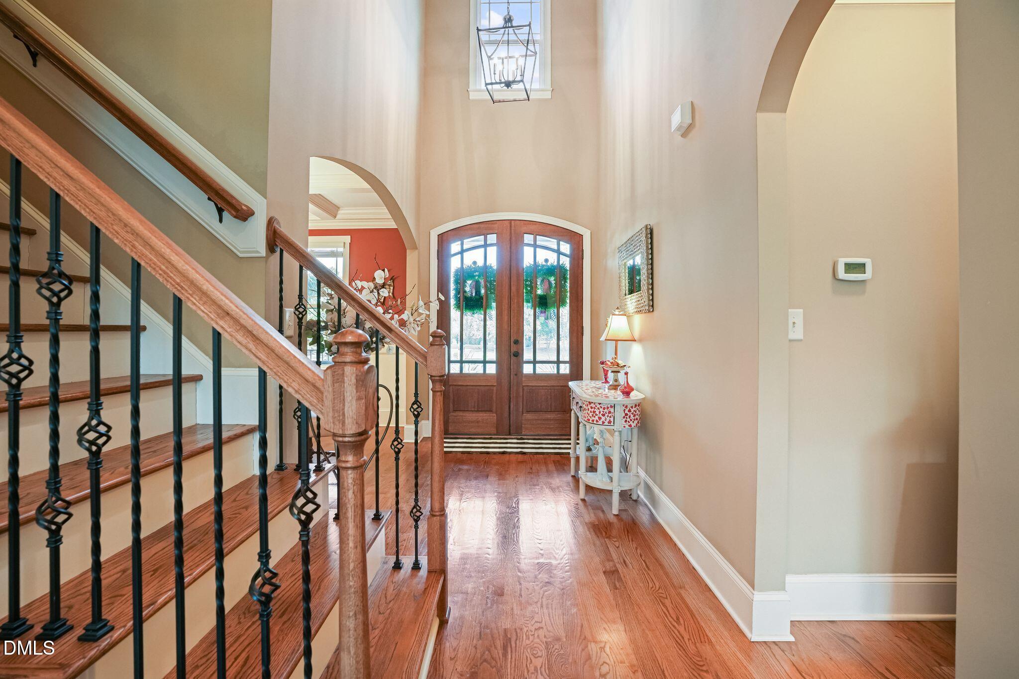 Two-story foyer with hardwood floors, an iron-and-wood staircase, and arched glass-paneled double doors.