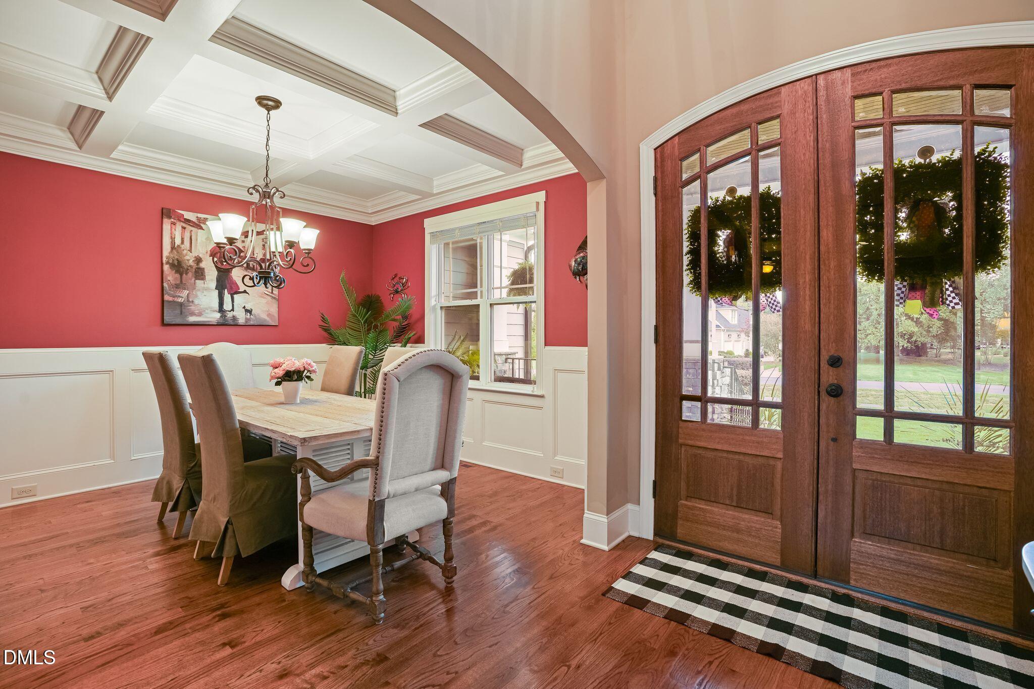 Dining room with a coffered ceiling, red walls, hardwood floors, and wood-and-glass entry doors.