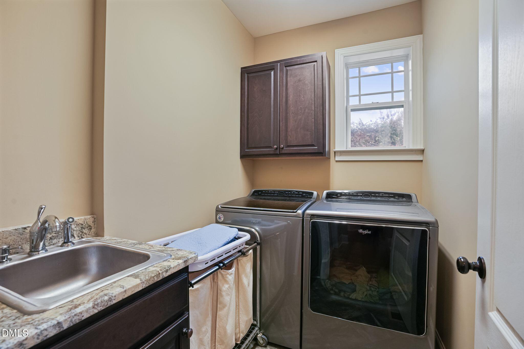 Laundry room with front-loading washer and dryer, utility sink, granite countertop, and window.