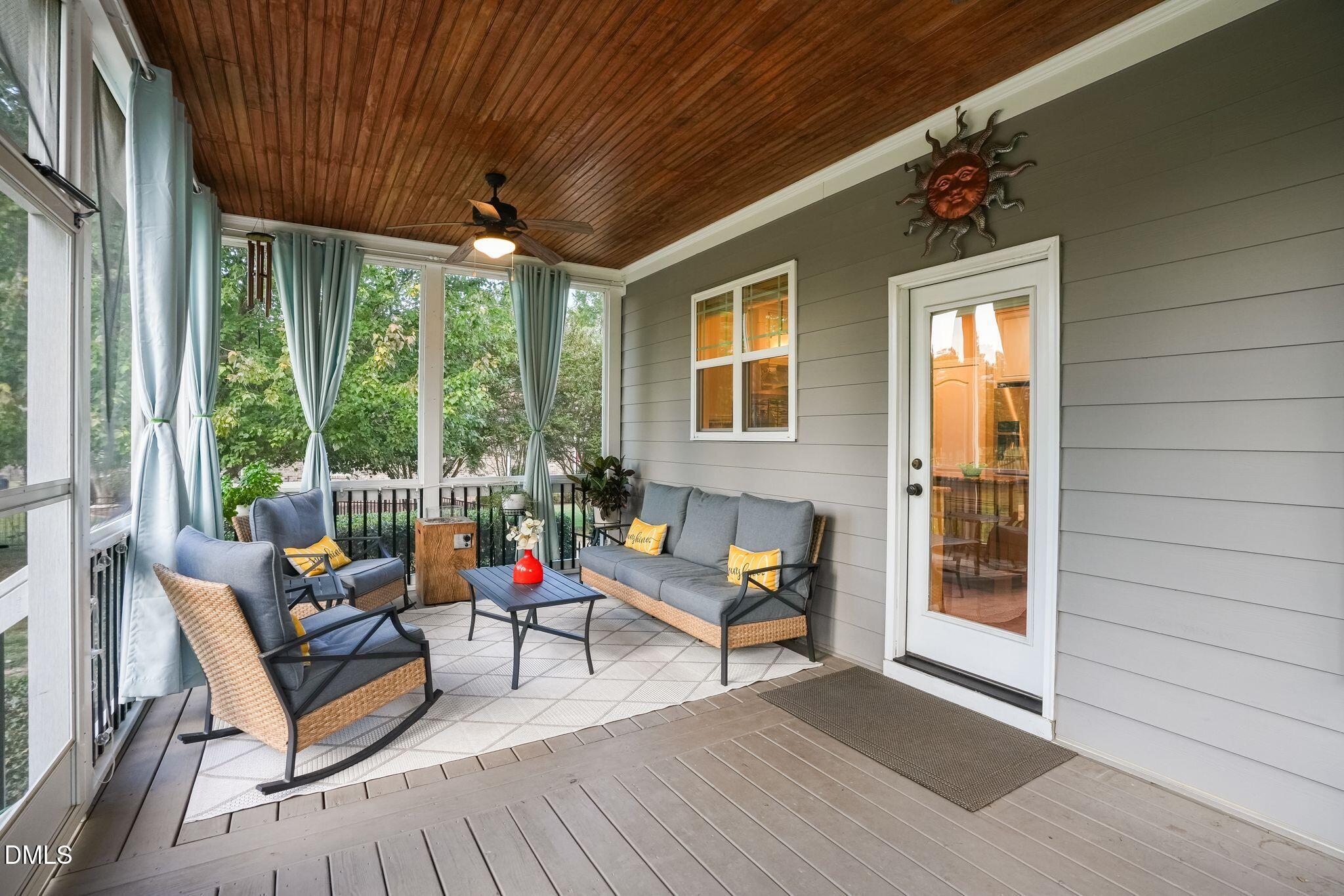 Screened porch with gray wicker seating, a wood-plank ceiling, and leafy tree views.