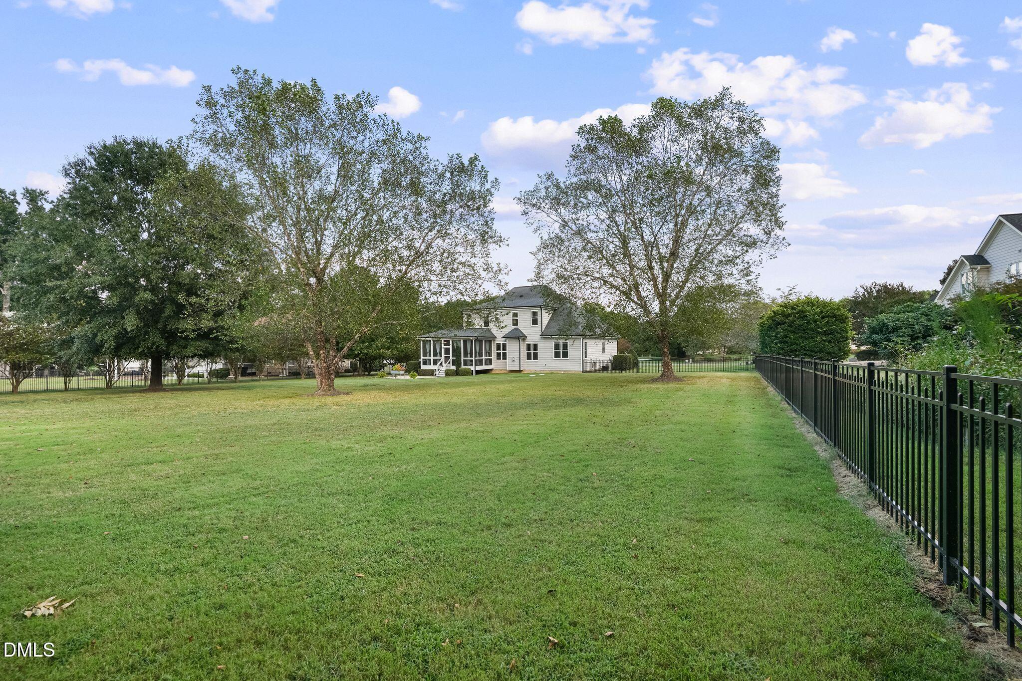 Spacious backyard with mature trees, a screened porch, and a black metal fence.