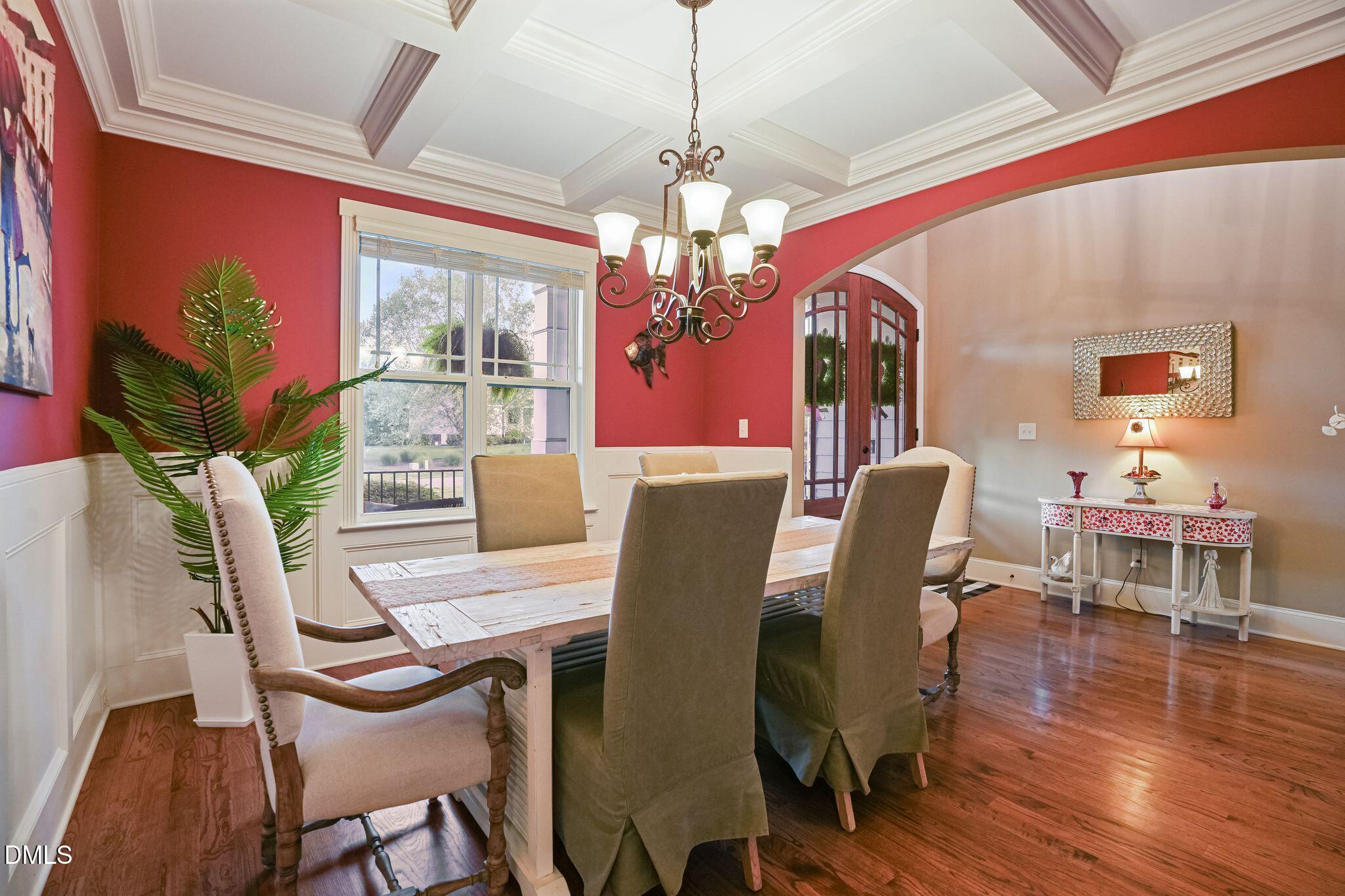 Dining room with a coffered ceiling, chandelier, red walls, and hardwood floors.