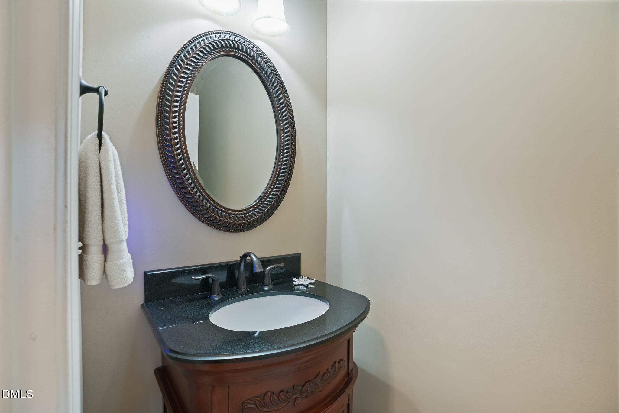 Bathroom vanity with a dark stone counter, carved wood cabinet, and ornate oval mirror.