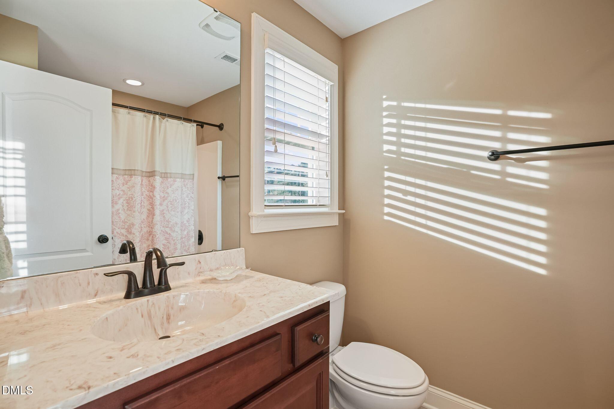 Bathroom with a marble-look vanity, dark wood cabinetry, and sunlight striping the tan wall.
