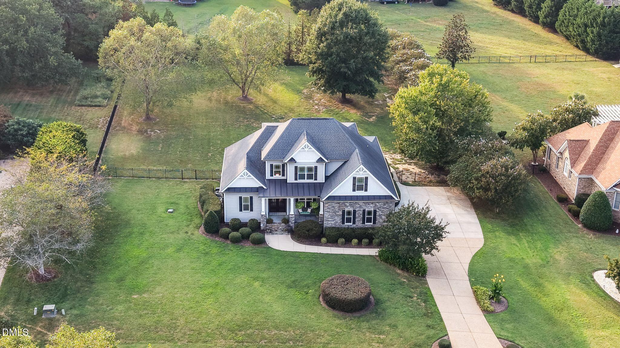 Aerial view of a gray-and-stone two-story home with a curved driveway, spacious lawn, and fenced backyard.