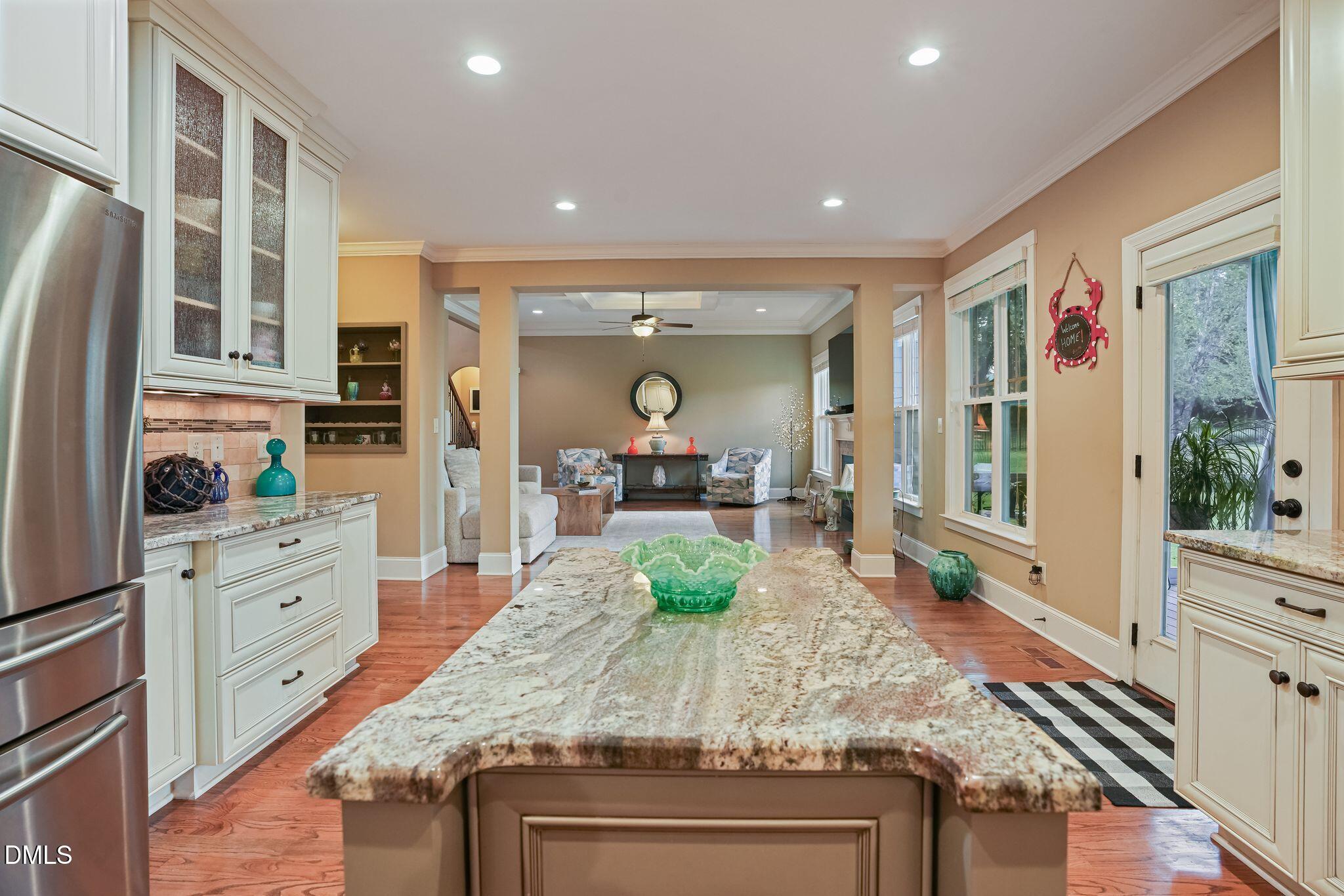Kitchen with a large granite island and white cabinets opening into a furnished living room.