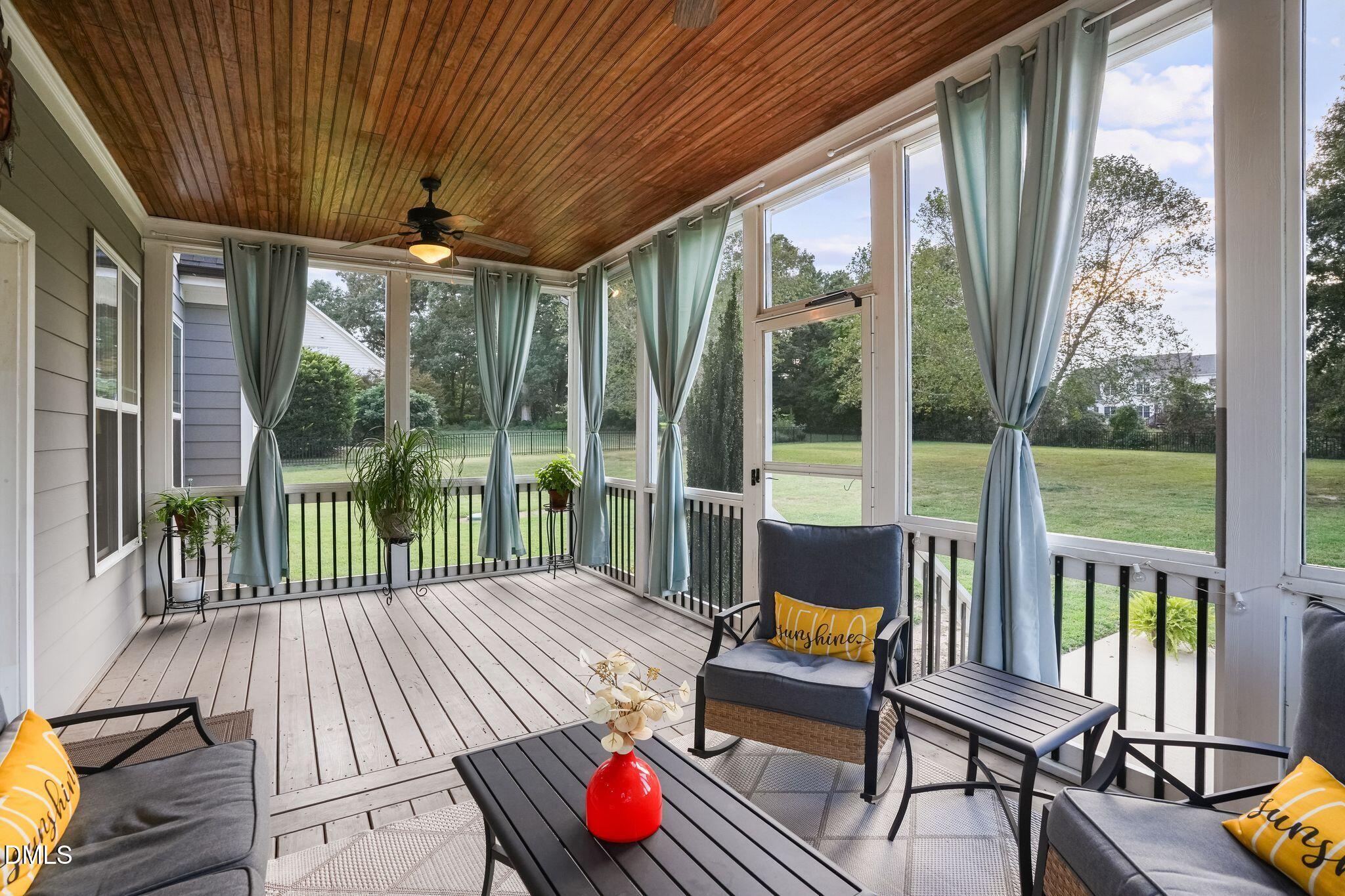 Screened porch with a wood ceiling, blue curtains, and seating overlooking a lawn.