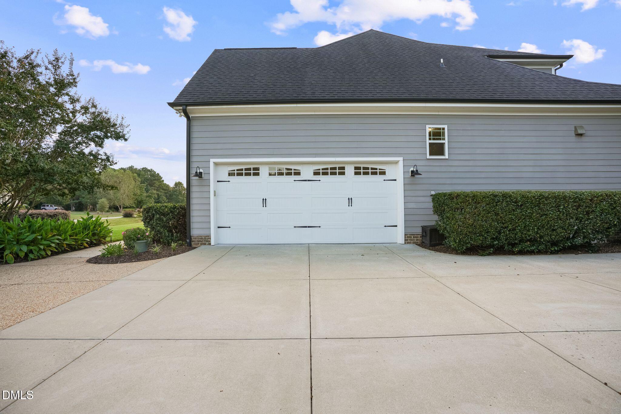 Gray-sided home with a white double garage door and broad concrete driveway.