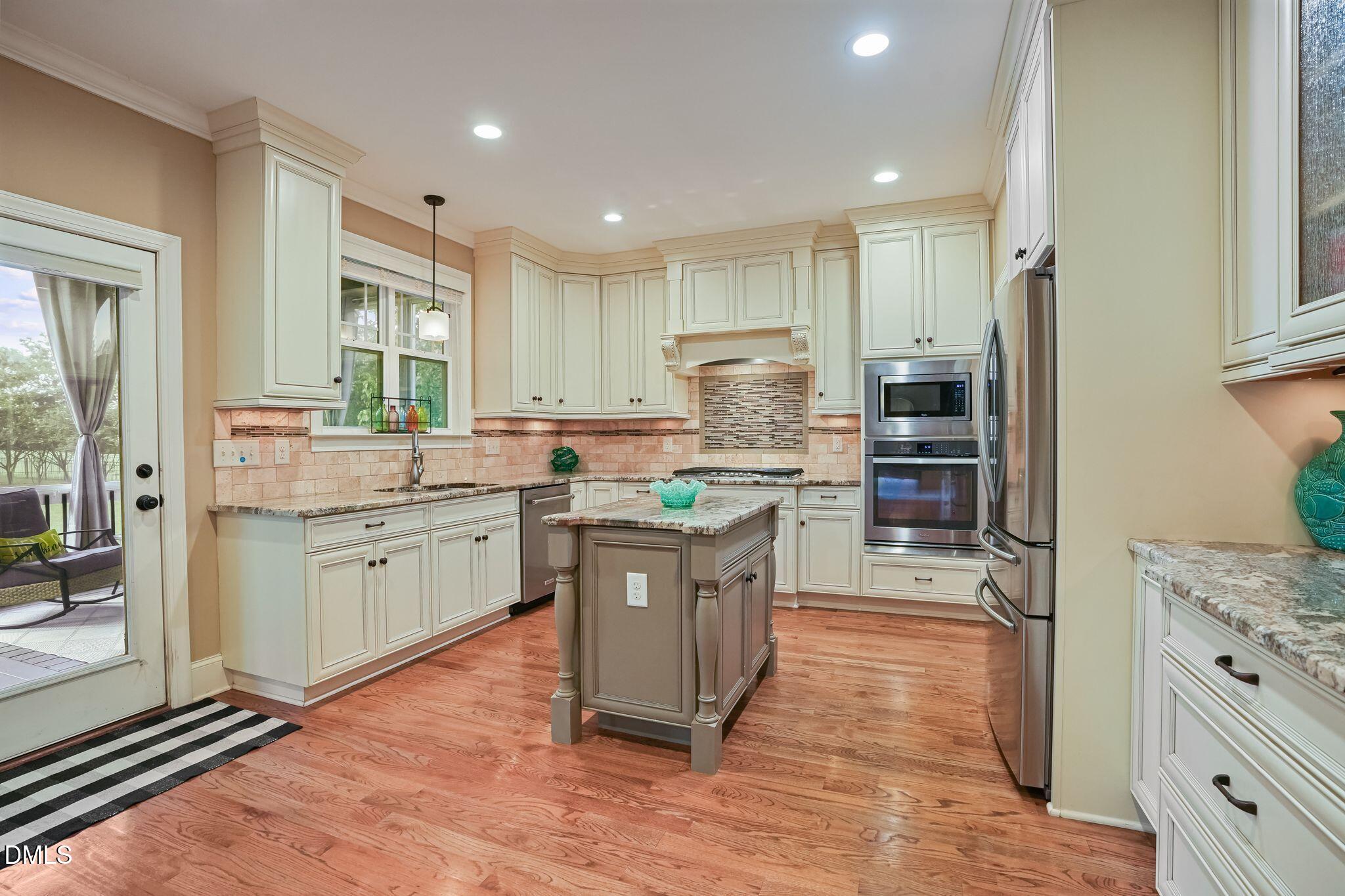 Kitchen with cream cabinetry, granite island, stainless steel appliances, and a glass door to the patio.