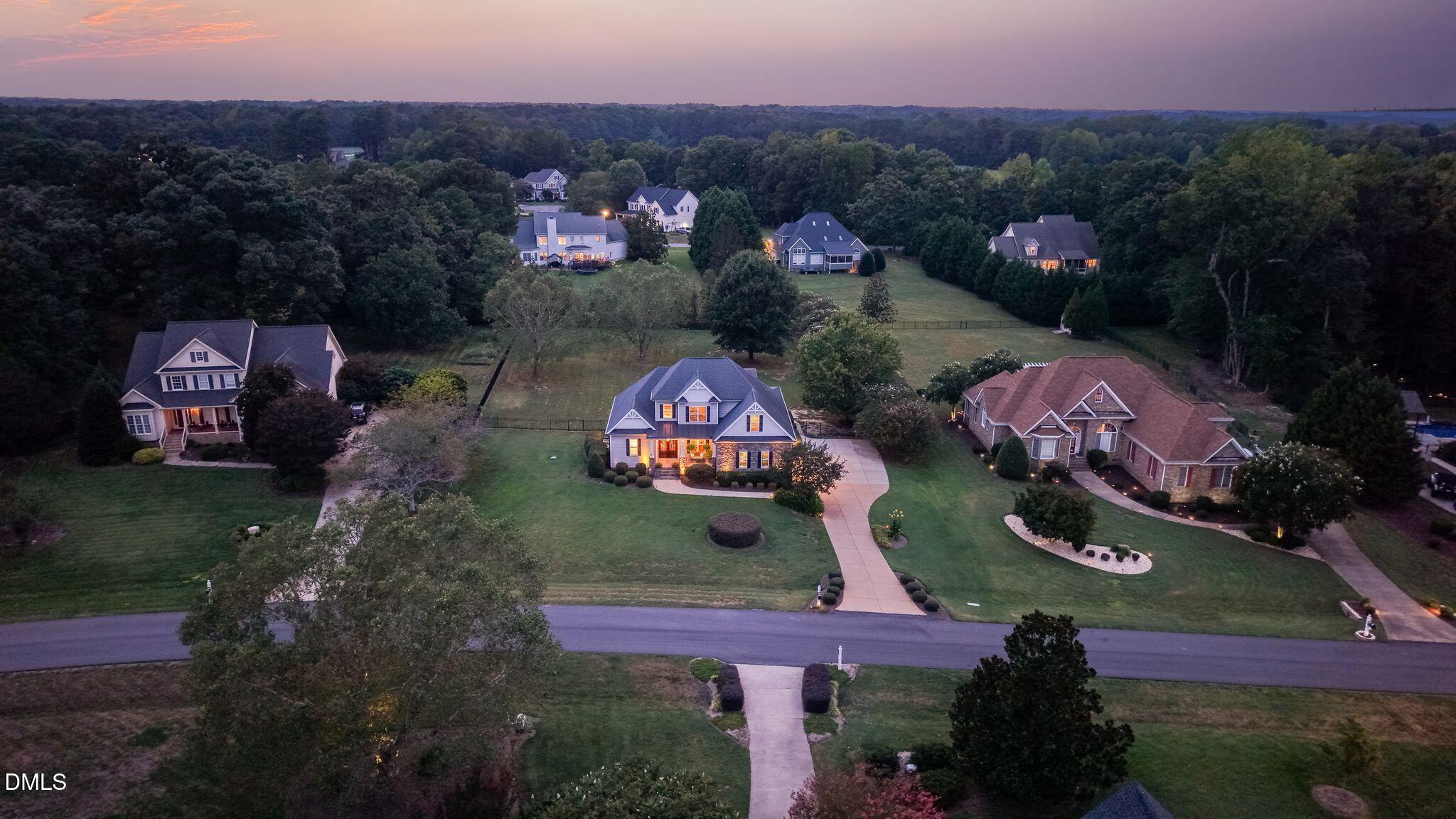 Aerial view of a lit two-story home and neighboring houses at dusk.